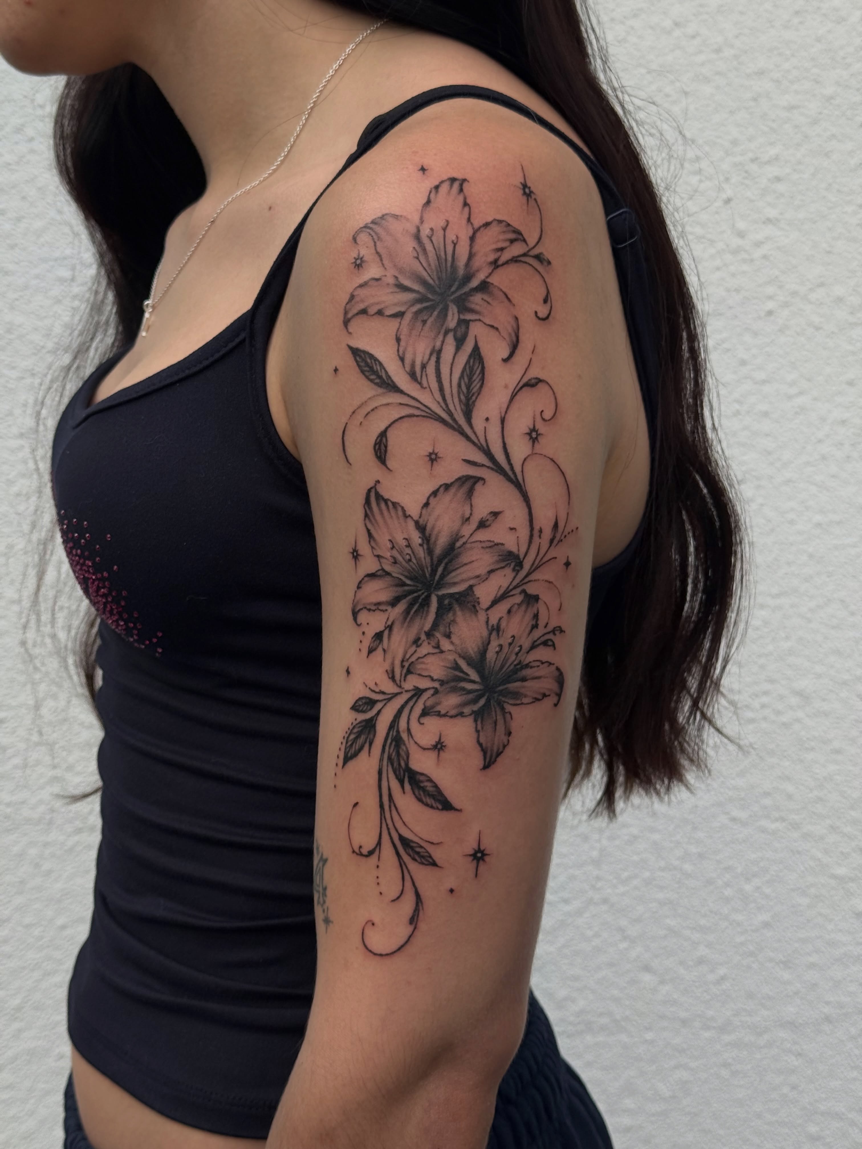 Lilies black and grey tattoo on the upper arm by Ava Nilou