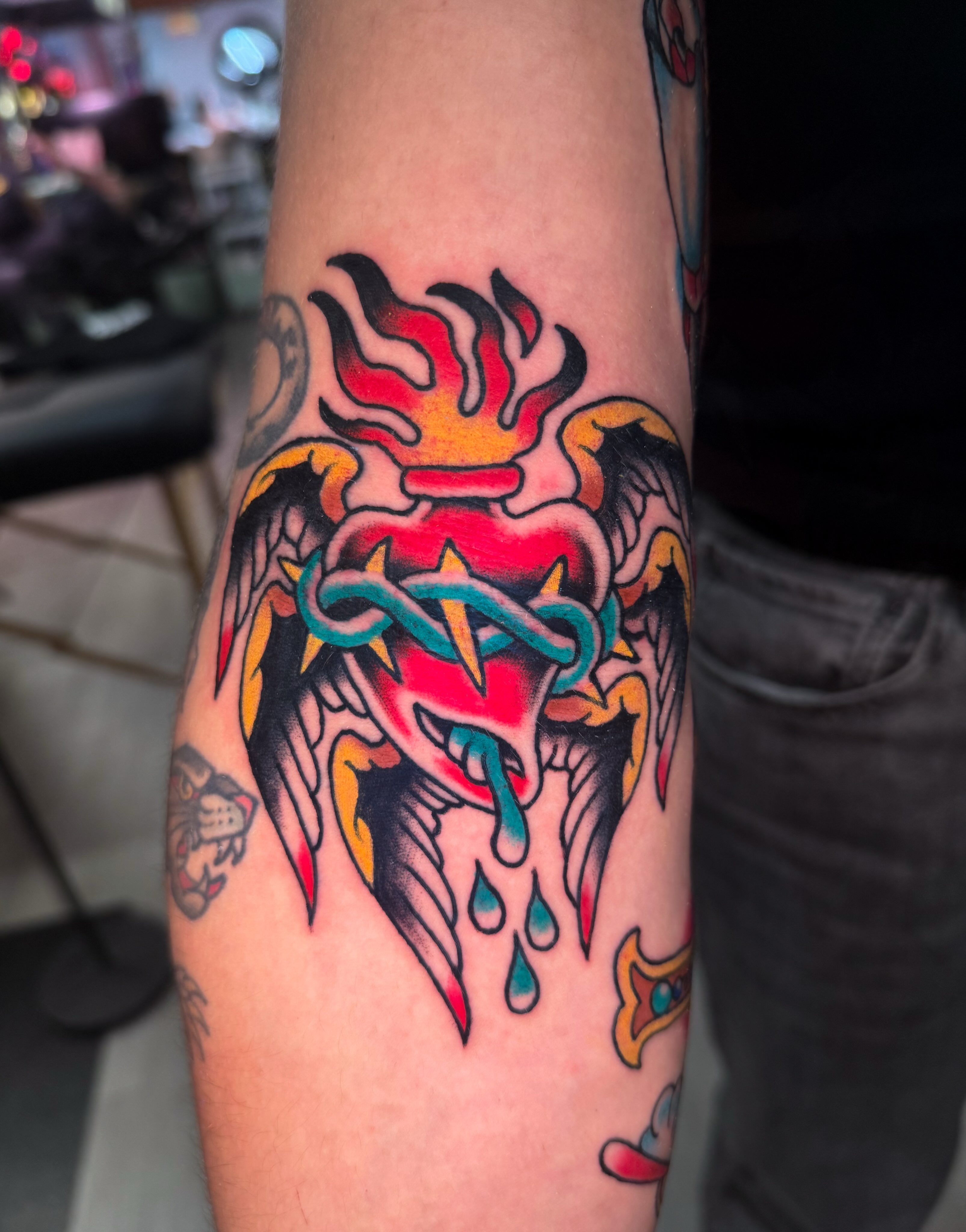 Heart with flames and wings American traditional tattoo on the forearm by Louie Flores
