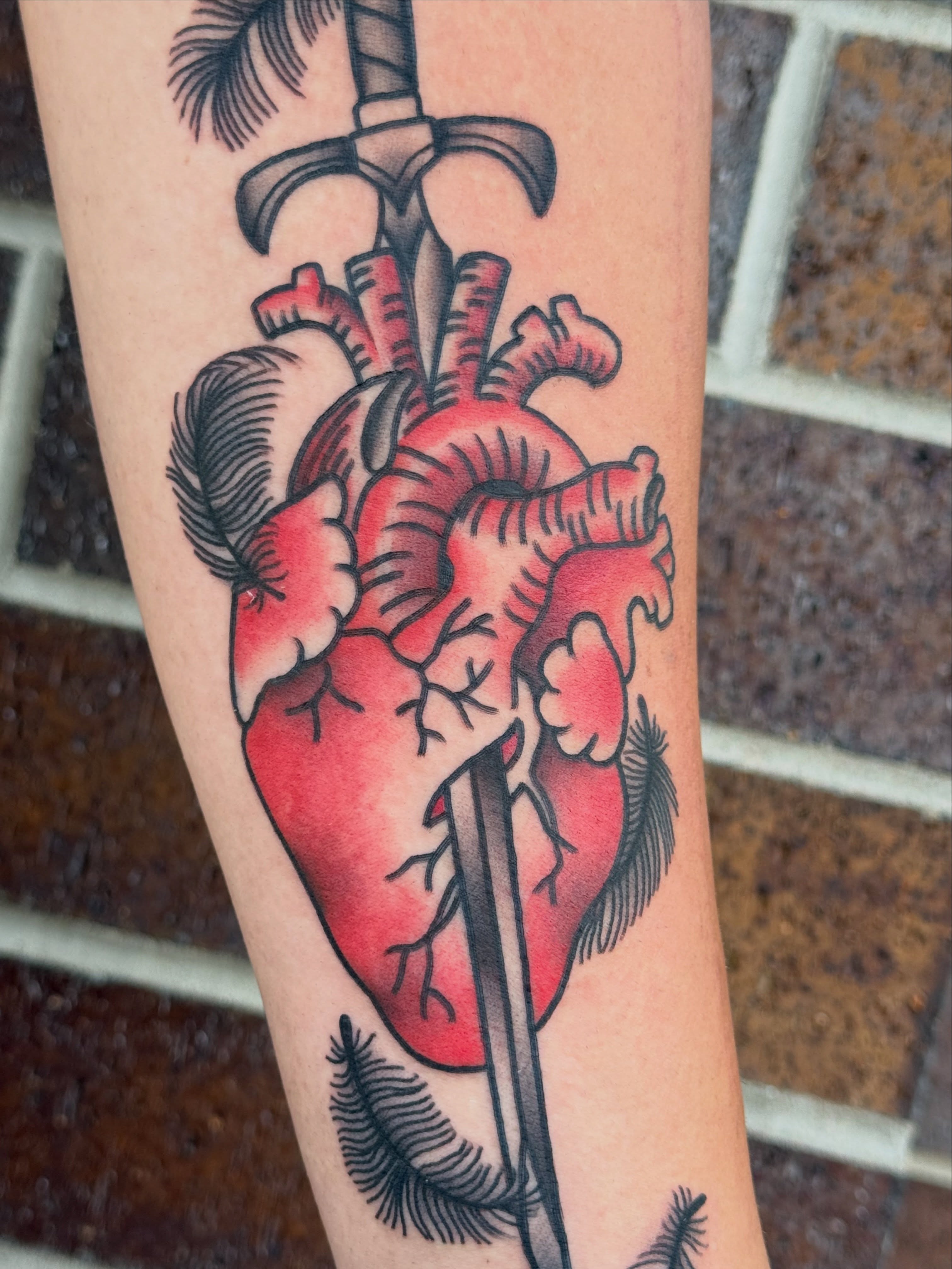 Heart with sword American traditional tattoo on the forearm by Kelsey Louis, Iowa City, Iowa