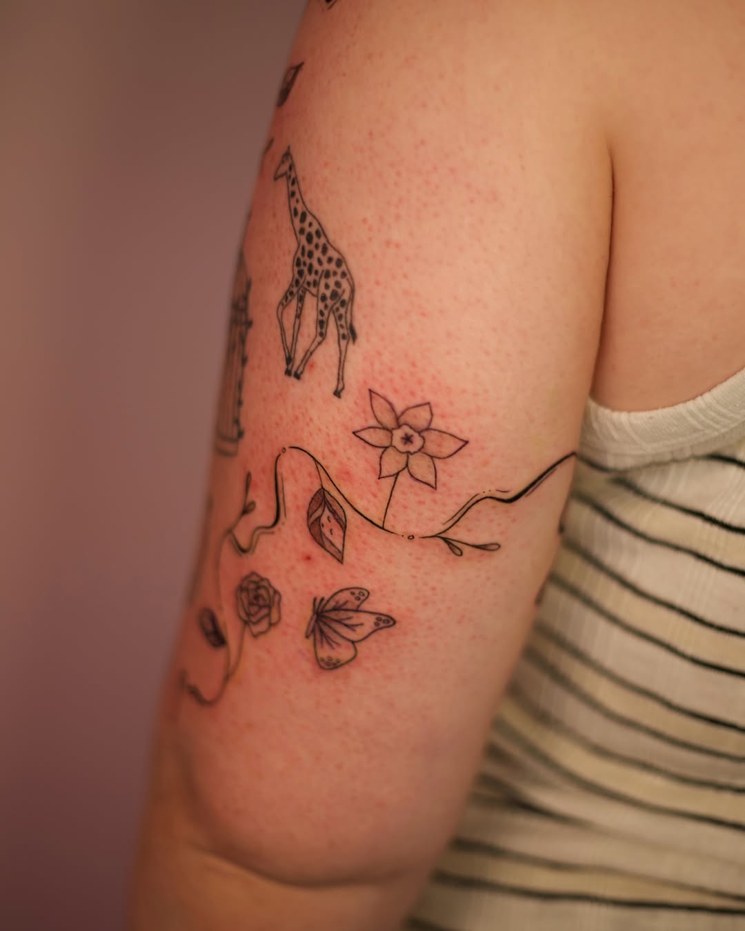 Giraffe and flower black and grey tattoo on the upper arm by Jess