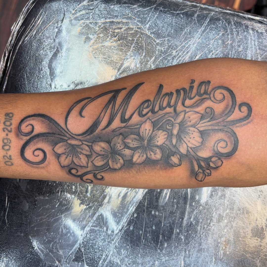 Name with floral design black and grey tattoo on the forearm by Sam Hearnen, Lawrence, Kansas