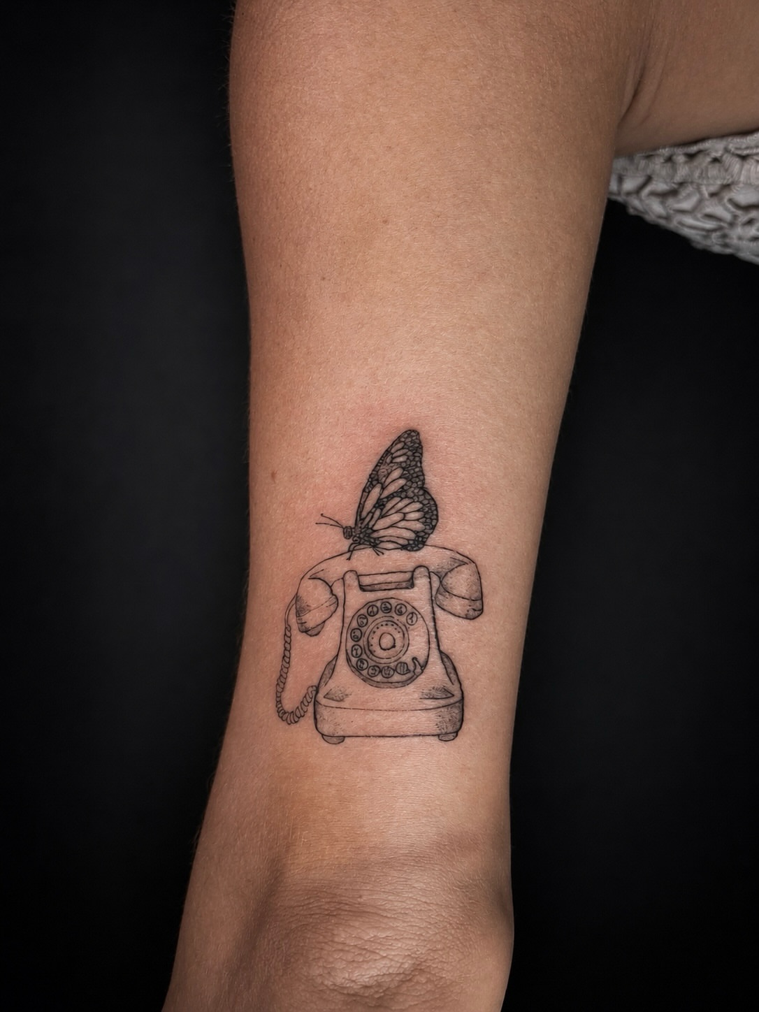 Telephone and butterfly black and grey tattoo on the forearm by 𝚃𝙰𝚃𝚃𝙾𝙾 𝙰𝚁𝚃𝙸𝚂𝚃, Charlotte, North Carolina