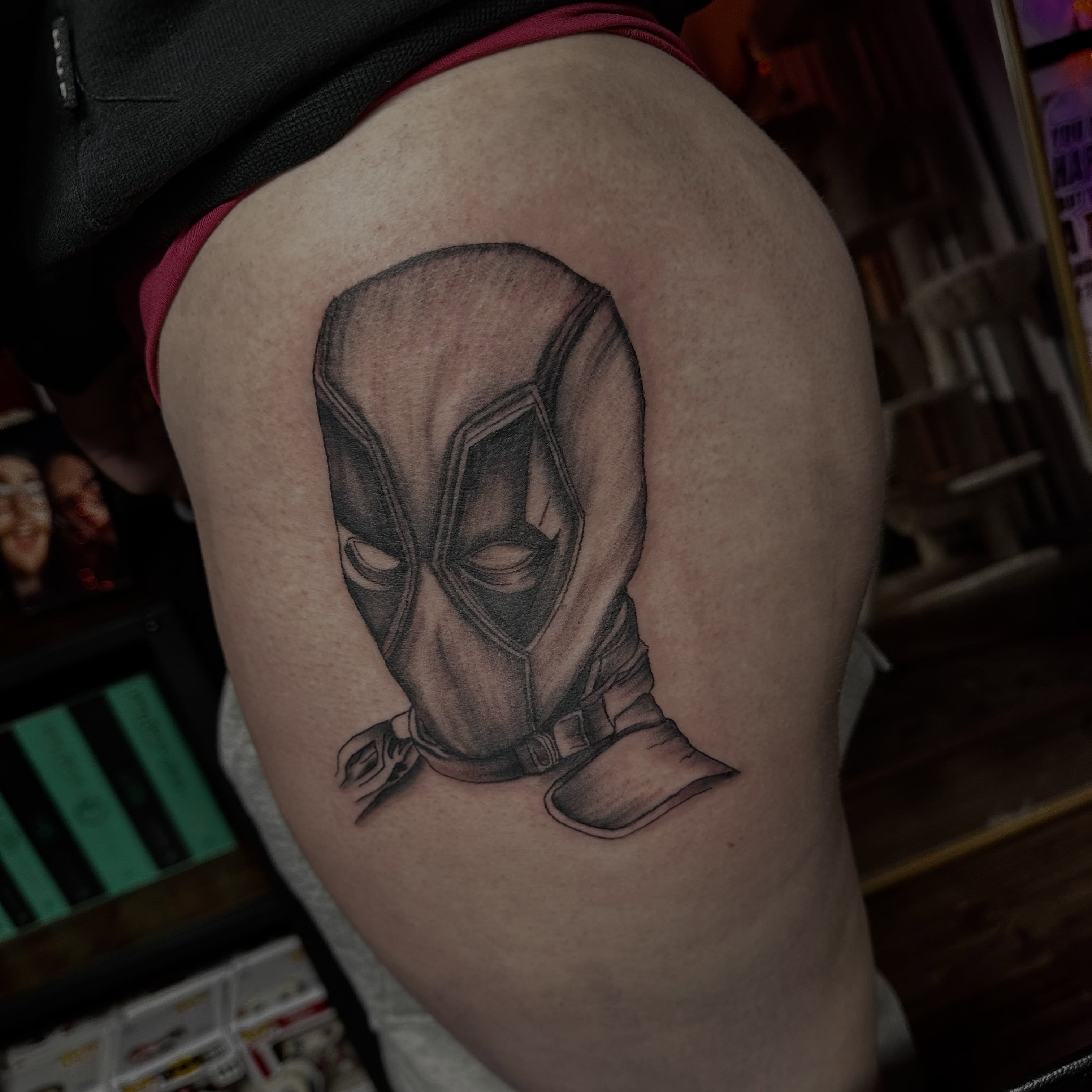 Deadpool mask black and grey tattoo on the thigh by Marly Quinn