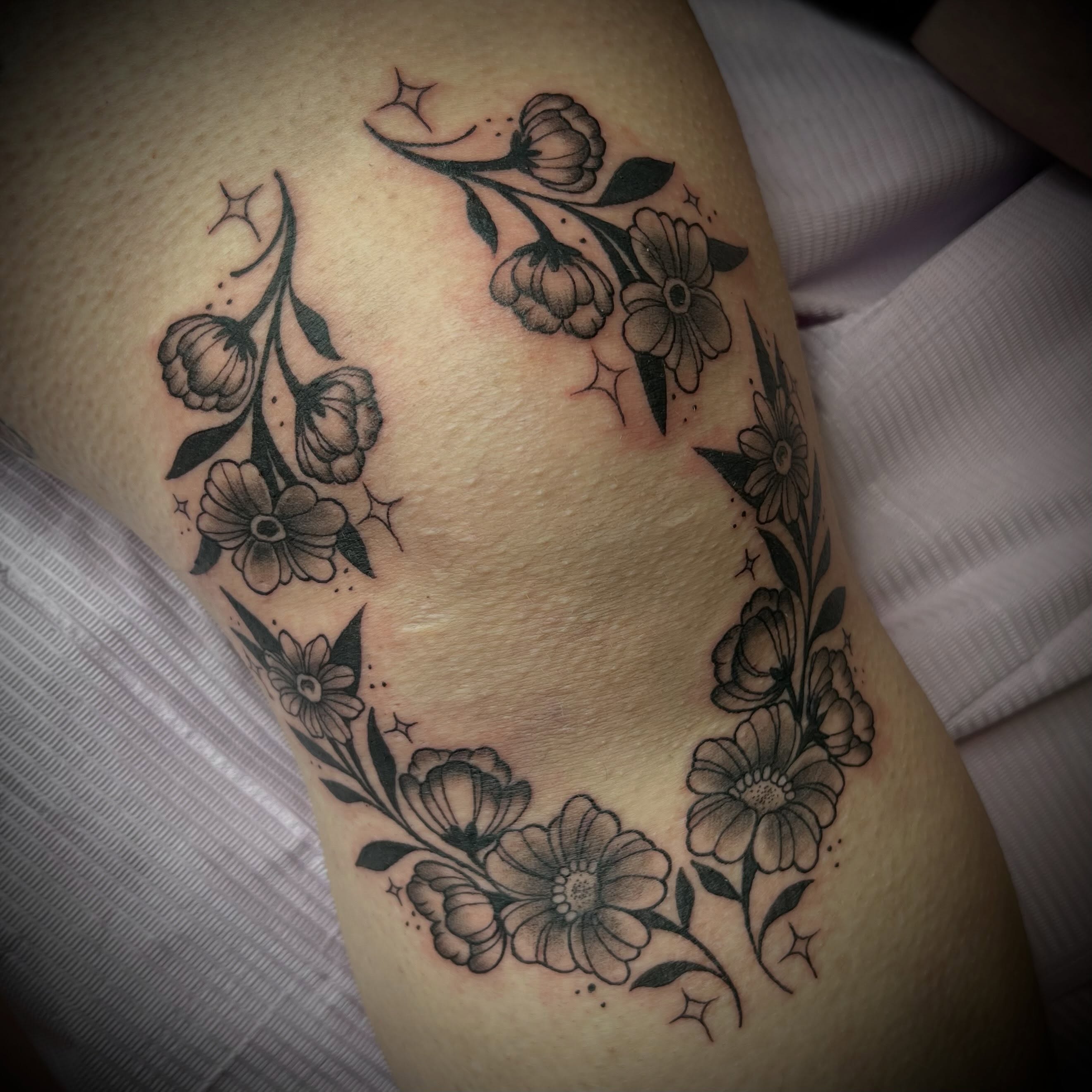 Floral wreath black and grey tattoo on the thigh by Ash Wheeler