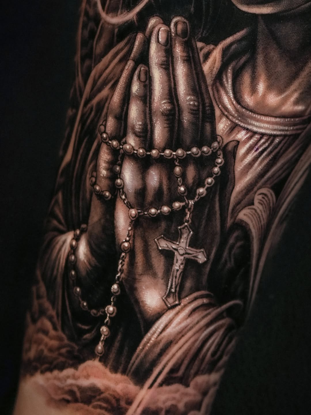 Praying hands with rosary Chicano tattoo on the upper arm by Sumok Kim