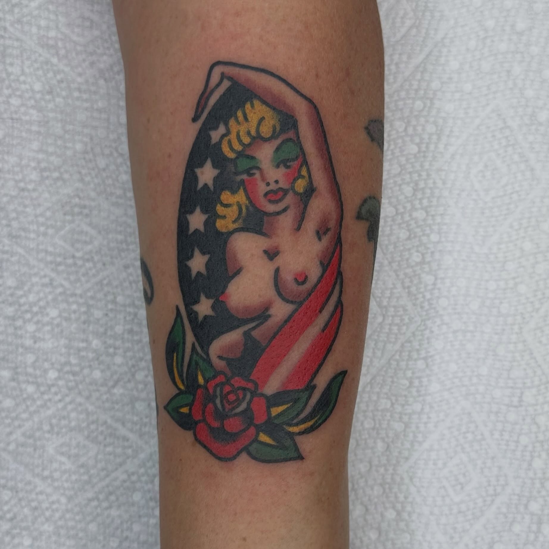 Nude woman with stars and stripes American traditional tattoo on the forearm by Keon Ostby, Tempe, Arizona
