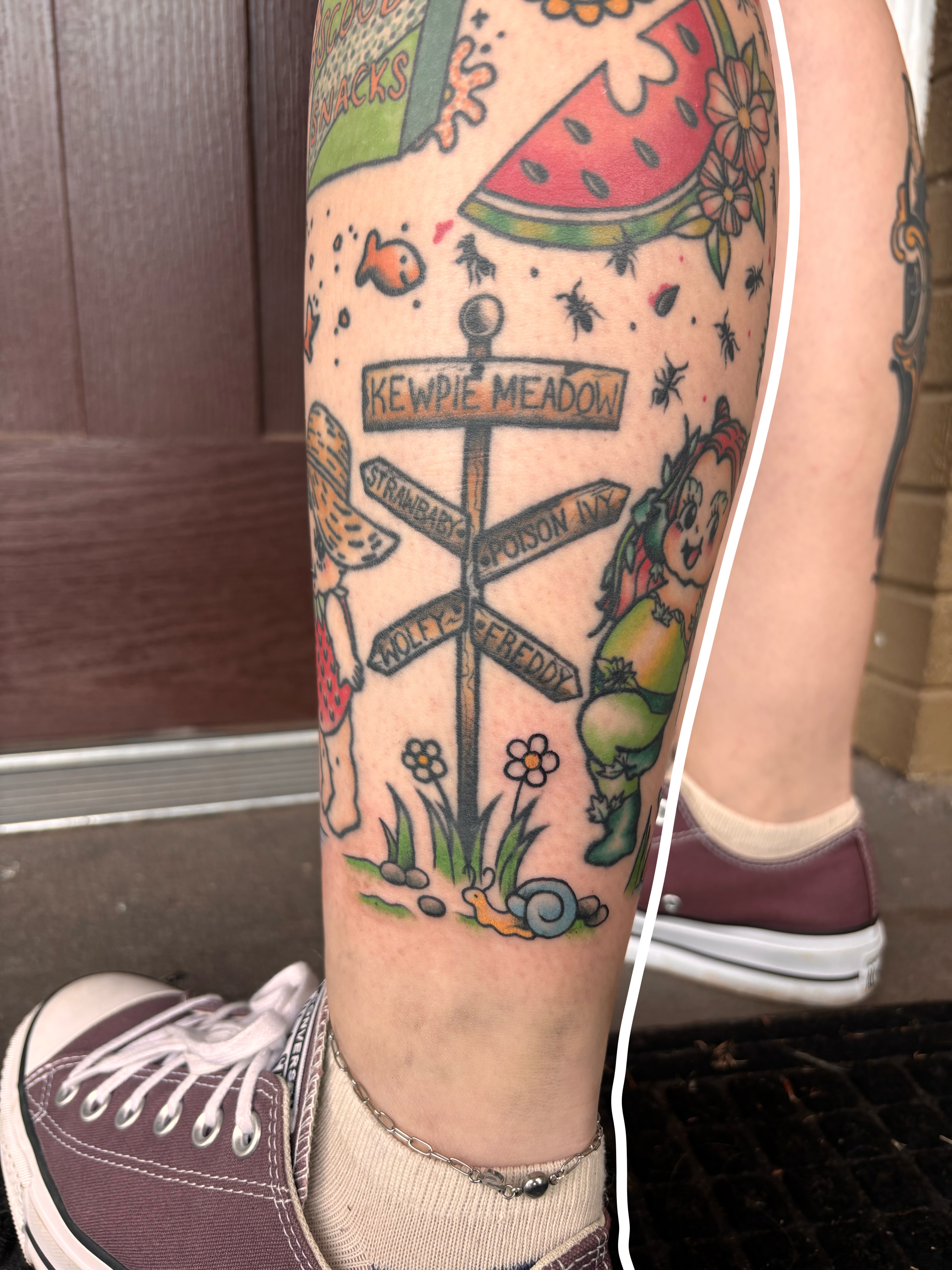 Signpost with cartoon characters new school tattoo on the forearm by Emmy Stepien