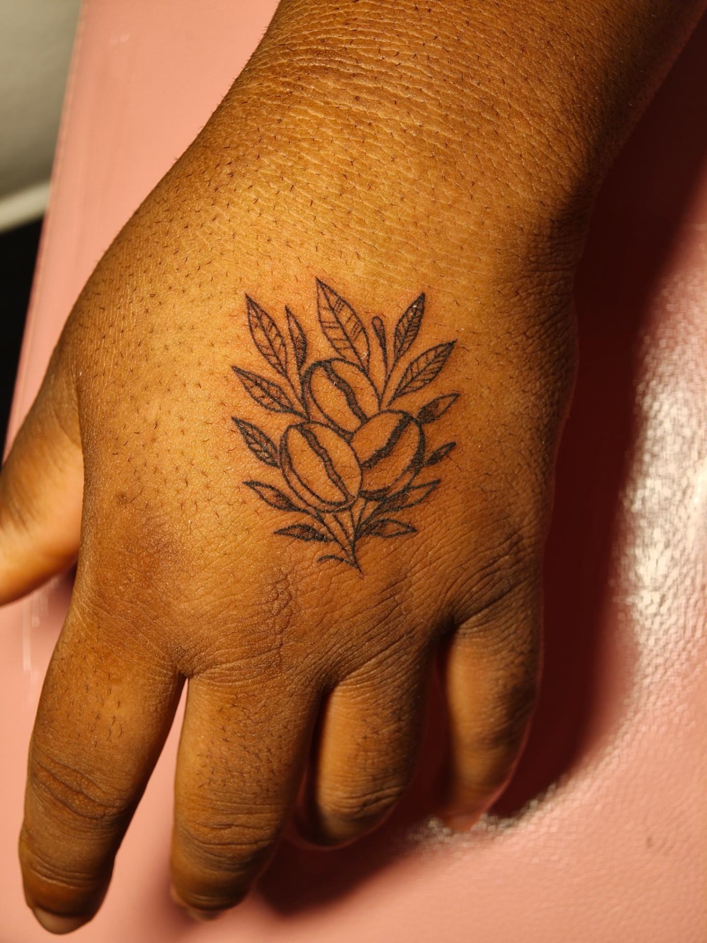 Coffee beans and leaves black and grey tattoo on the hand by Dani Sandoval, Anaheim, California