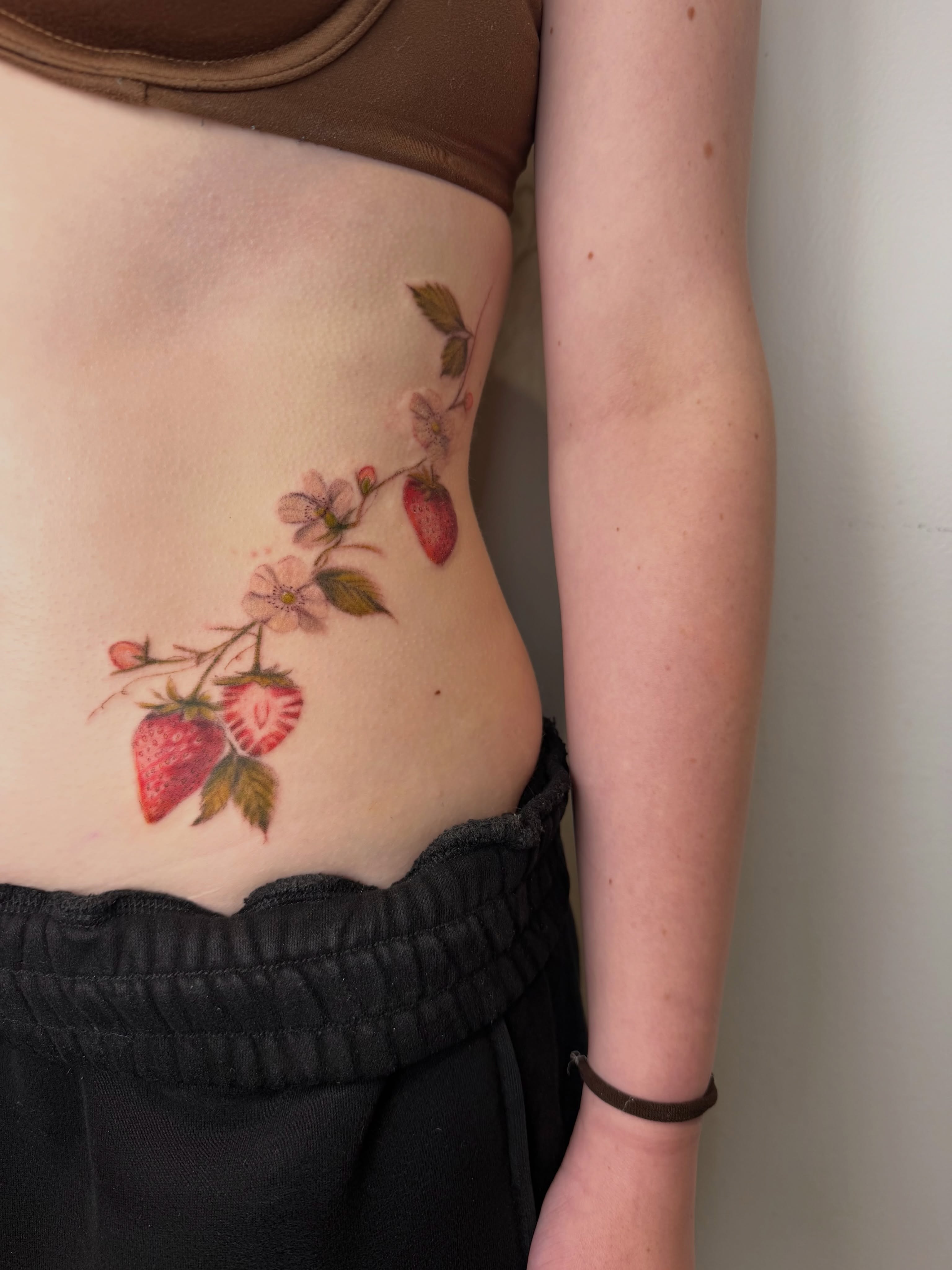 Strawberries and flowers watercolor tattoo on the ribs by Mackenzie