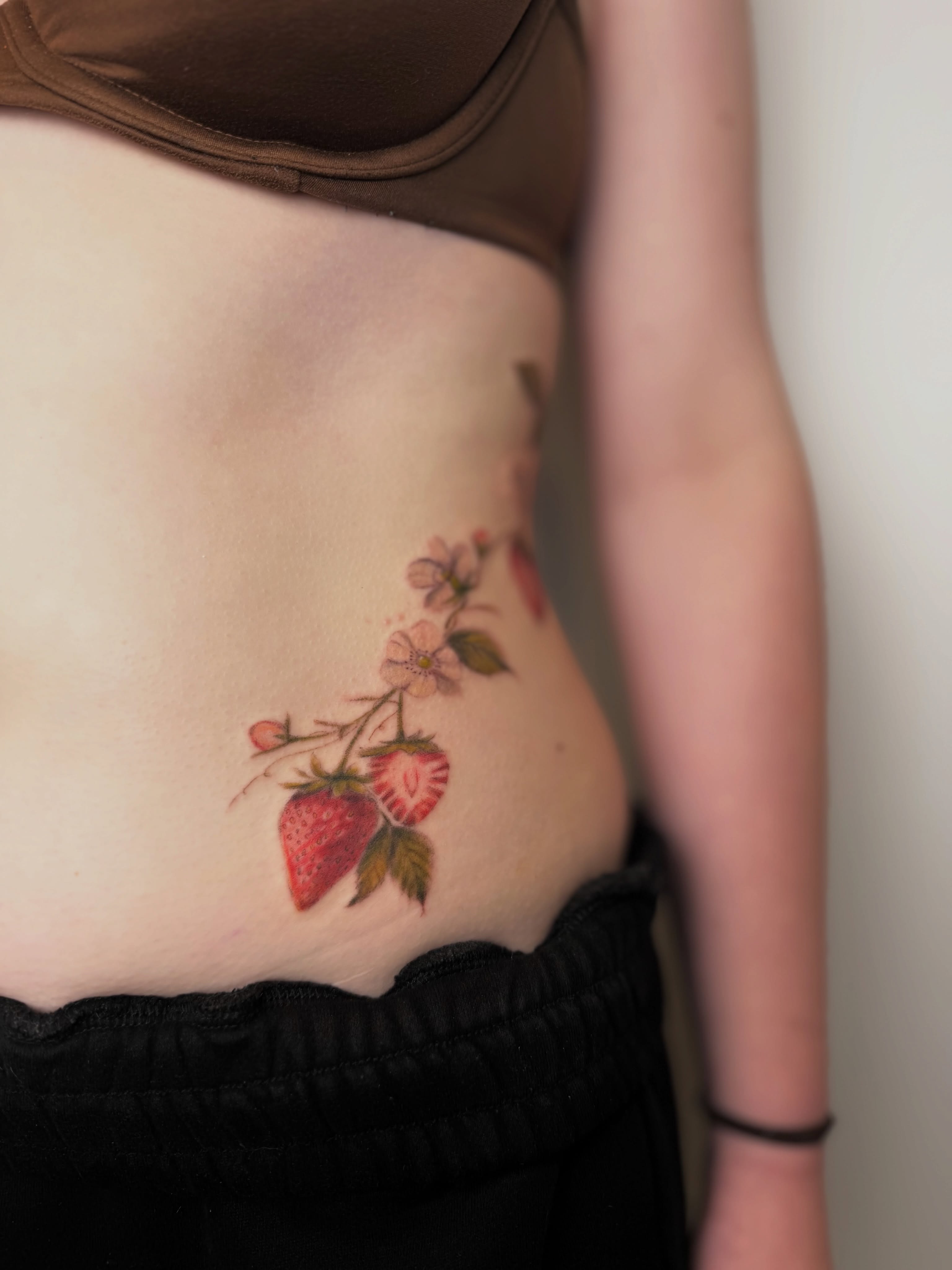 Strawberries and flowers realism tattoo on the ribs by Mackenzie