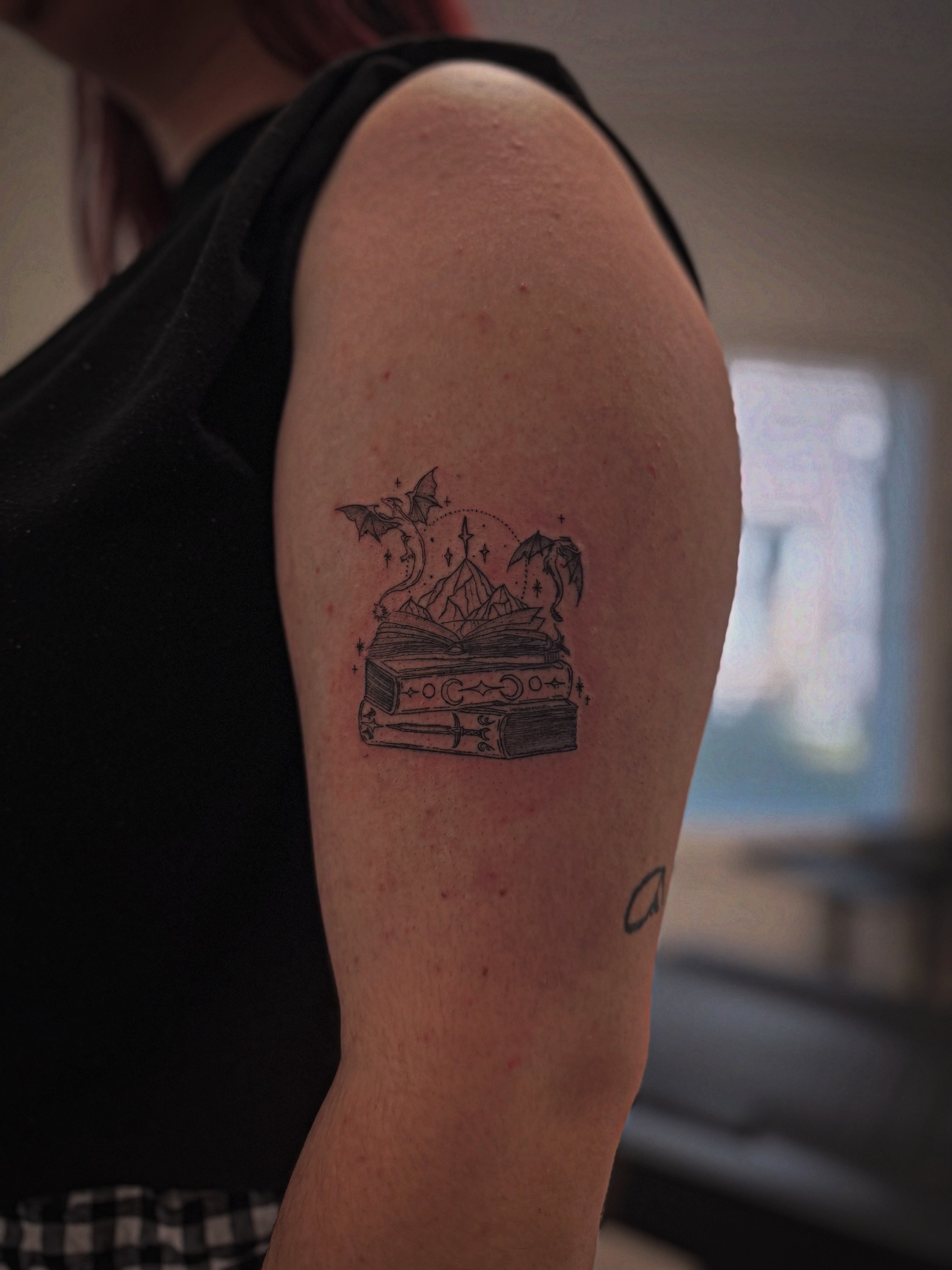 Book with magical elements black and grey tattoo on the upper arm by Taylor Johnson