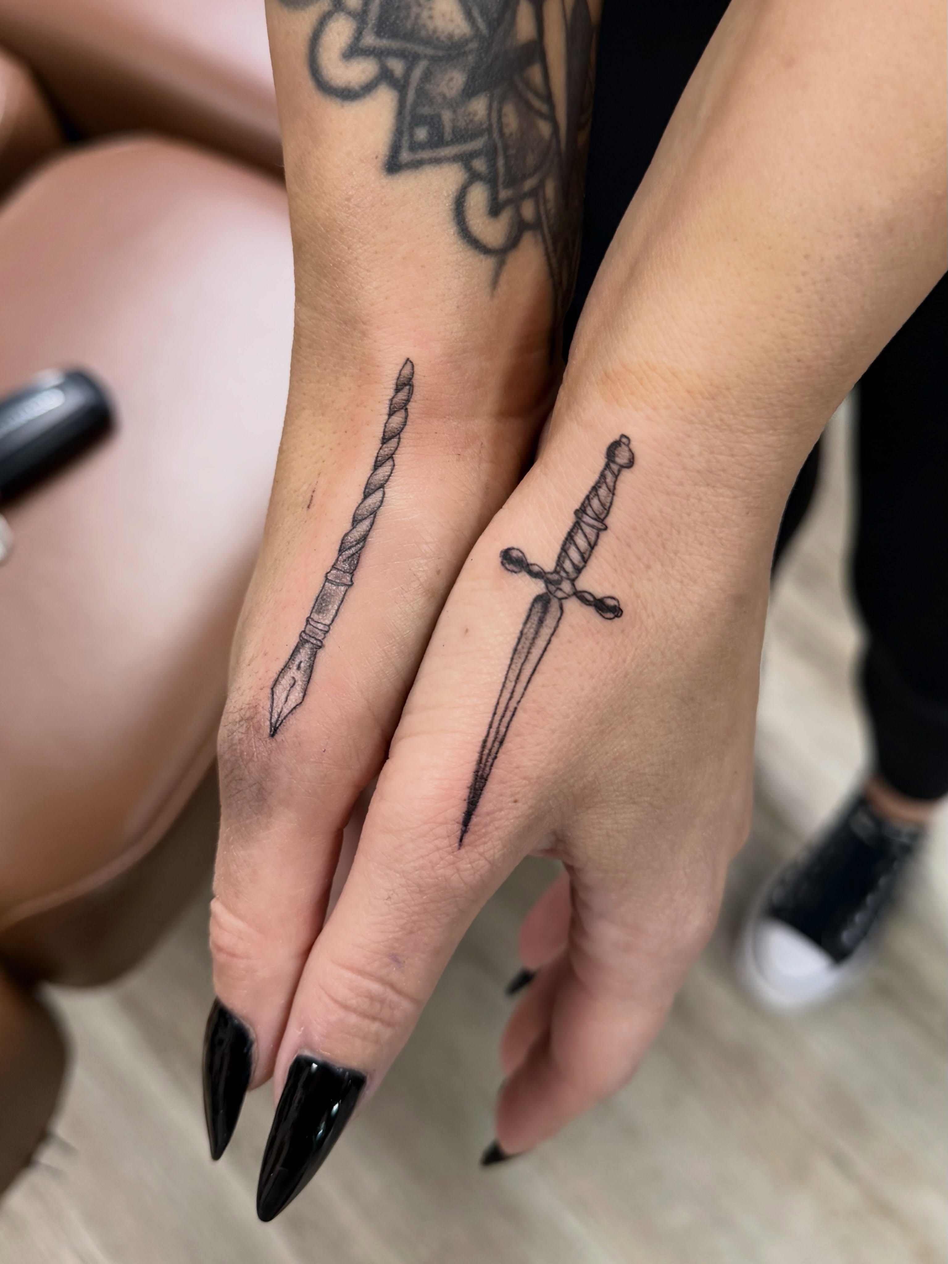 Pen and dagger black and grey tattoo on the hand by Bailee