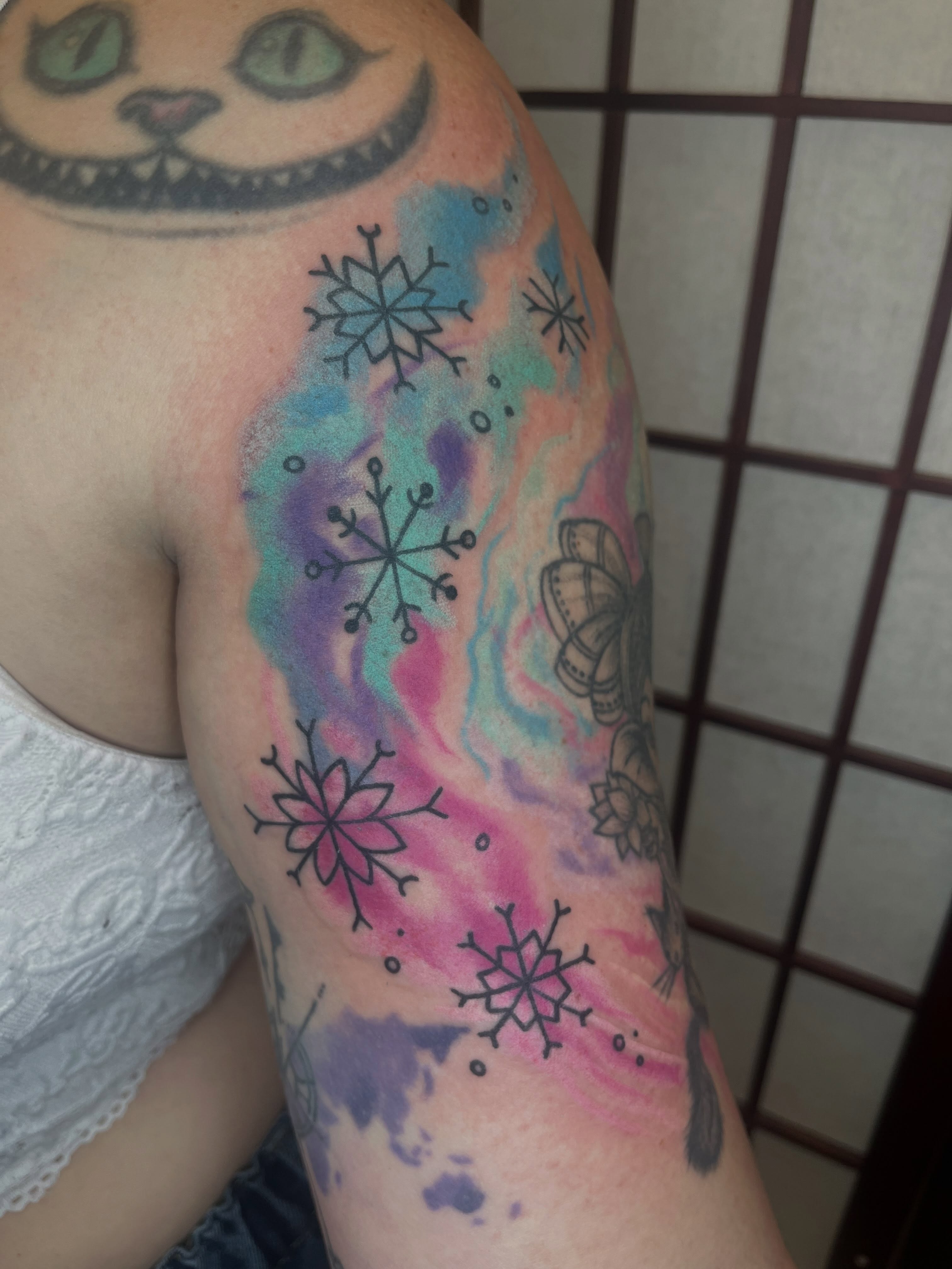 Snowflakes watercolor tattoo on the upper arm by Lauryn Dunkle