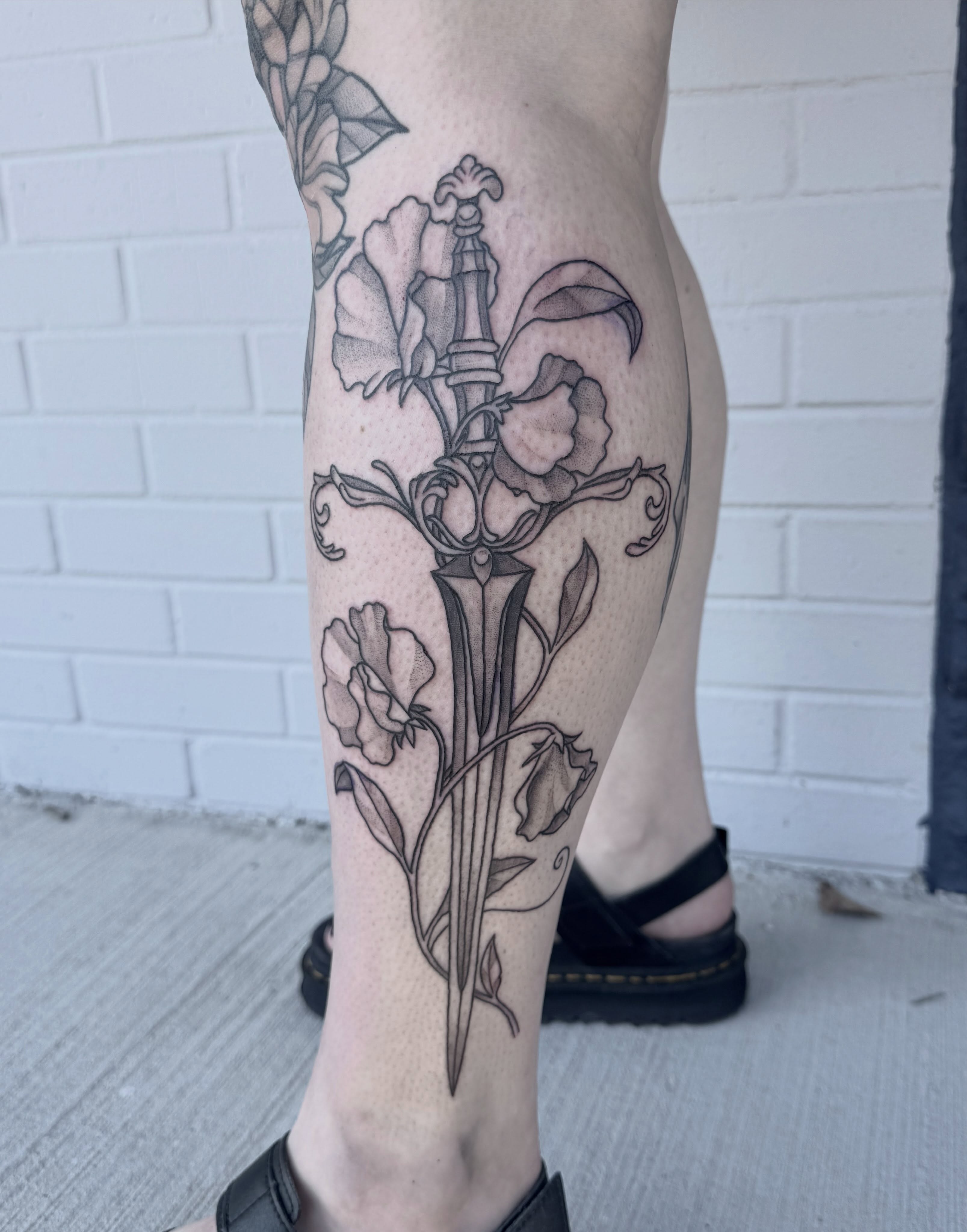 Sword and flowers ornamental tattoo on the calf by Audrey Kacel, Holland, Michigan