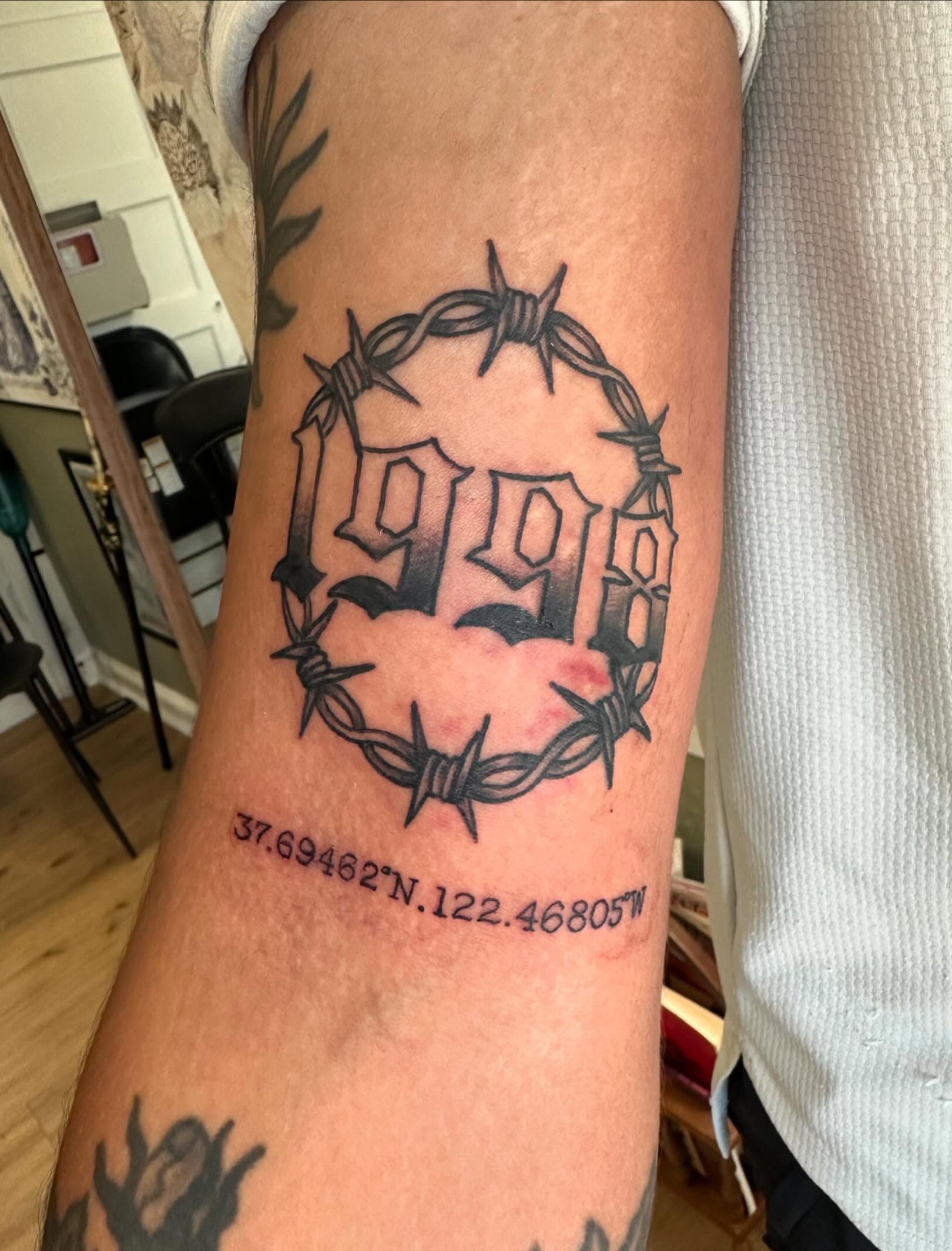Barbed wire and '1991' black and grey tattoo on the forearm by Kaylee Woods