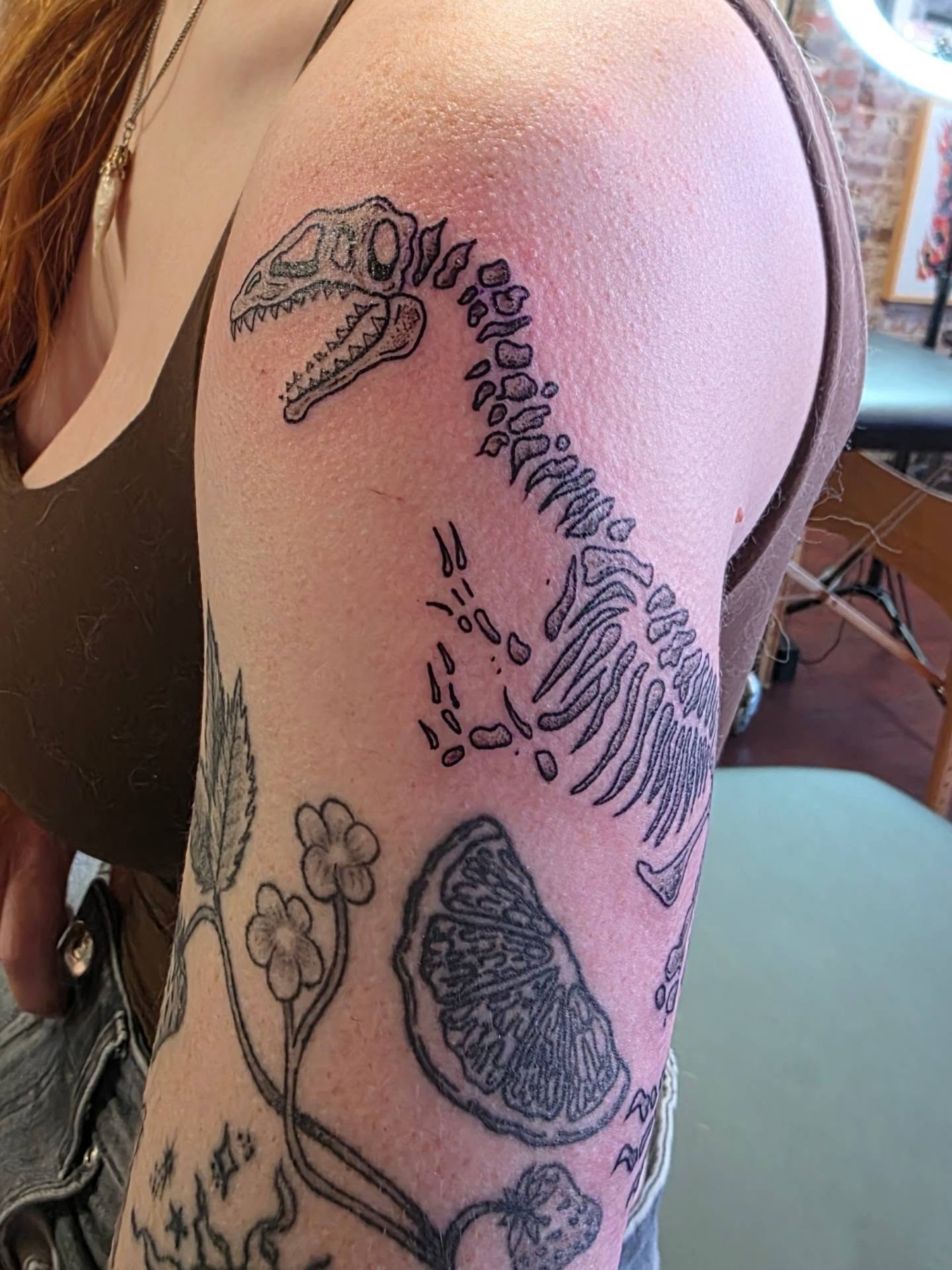 Dinosaur skeleton black and grey tattoo on the upper arm by Tattoos by Annie