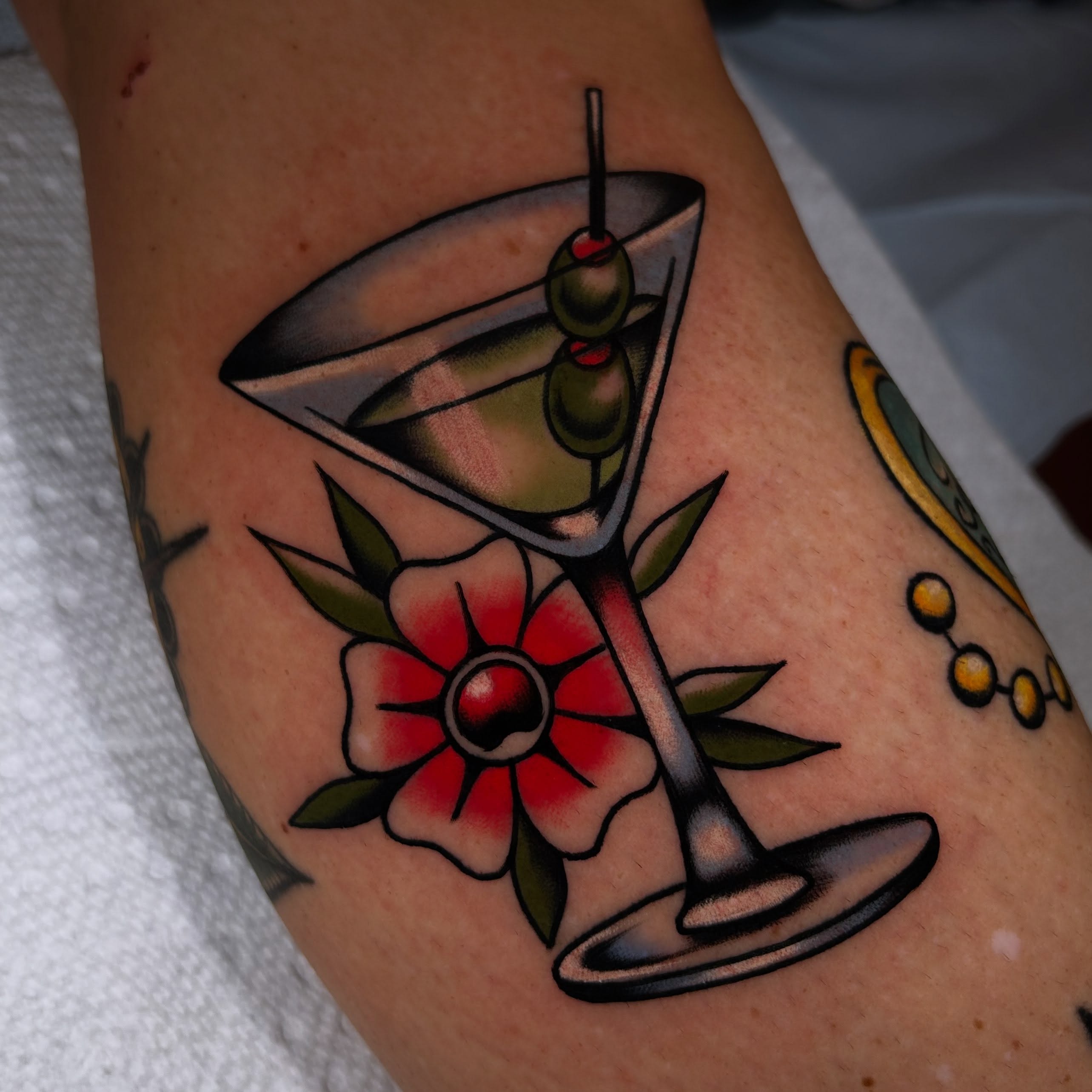 Martini glass with olives American traditional tattoo on the forearm by Lexi Kniskern