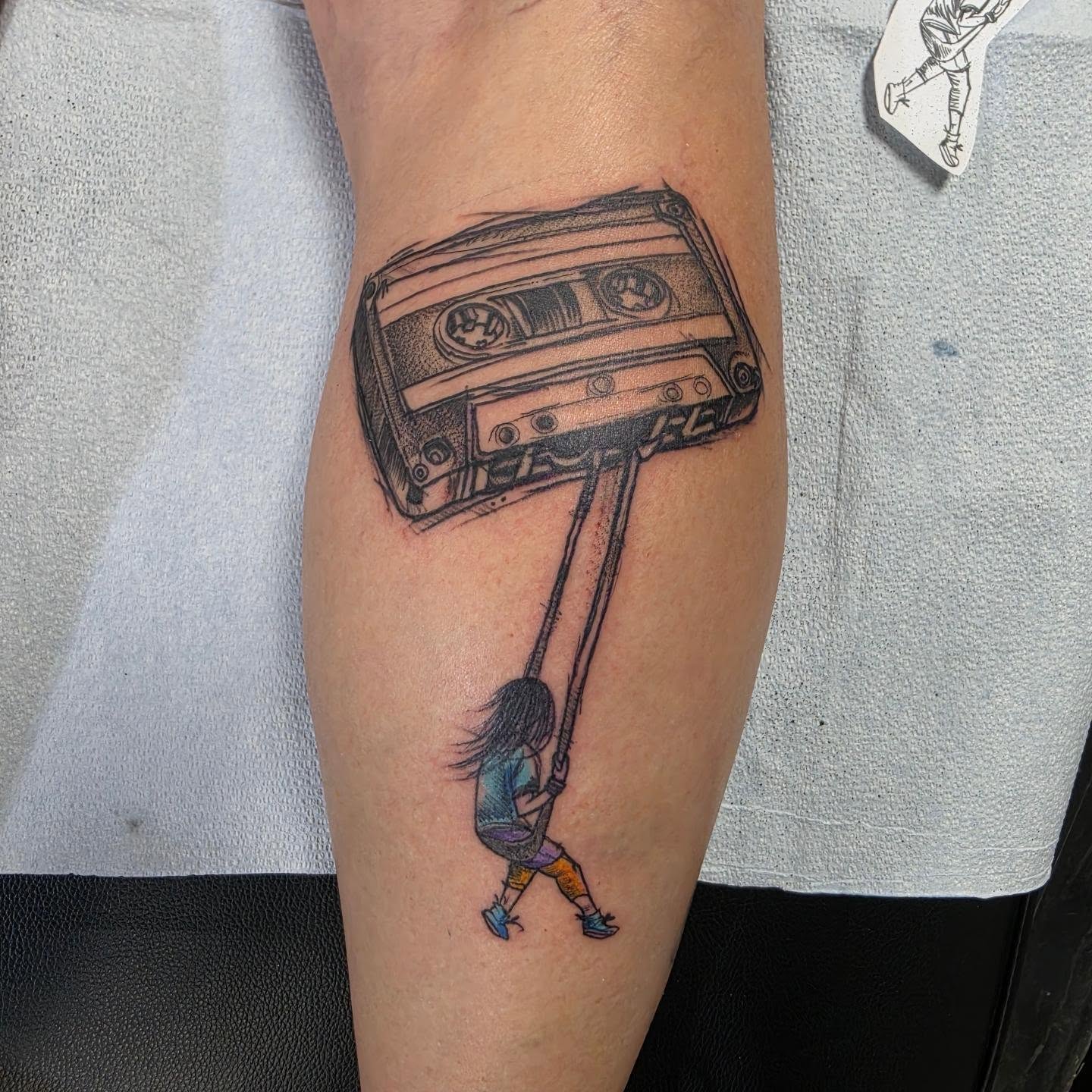 Cassette tape with girl black and grey tattoo on the forearm by Robert Glover
