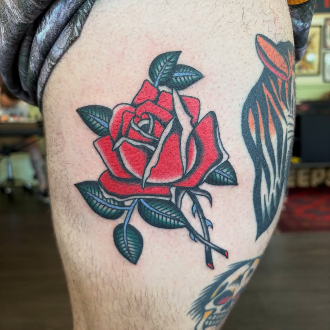 Red rose American traditional tattoo on the thigh by Izzy