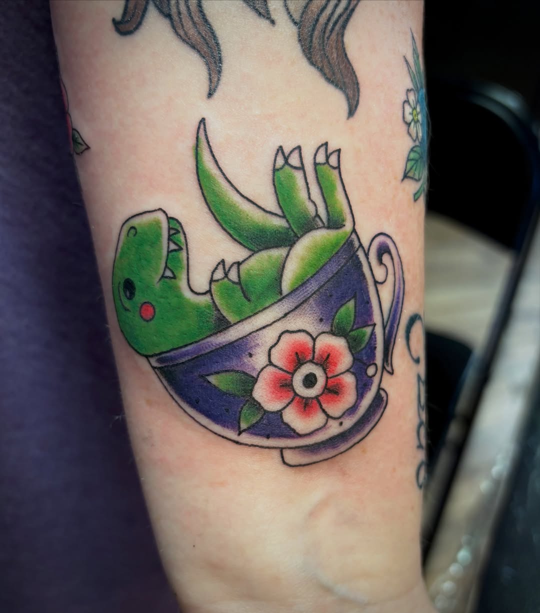 Dinosaur in teacup new school tattoo on the forearm by Reid