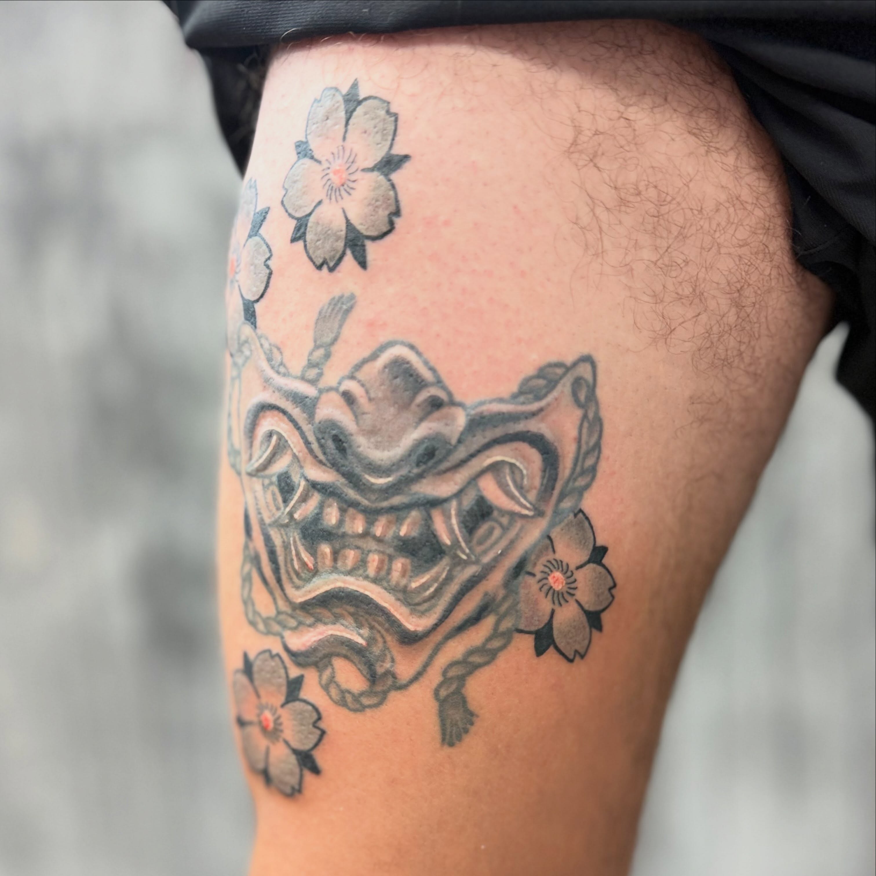 Mask and cherry blossoms black and grey tattoo on the thigh by Camilo
