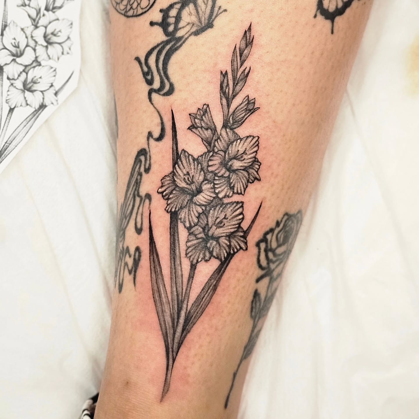 Gladiolus flowers black and grey tattoo on the leg by Lili Gu