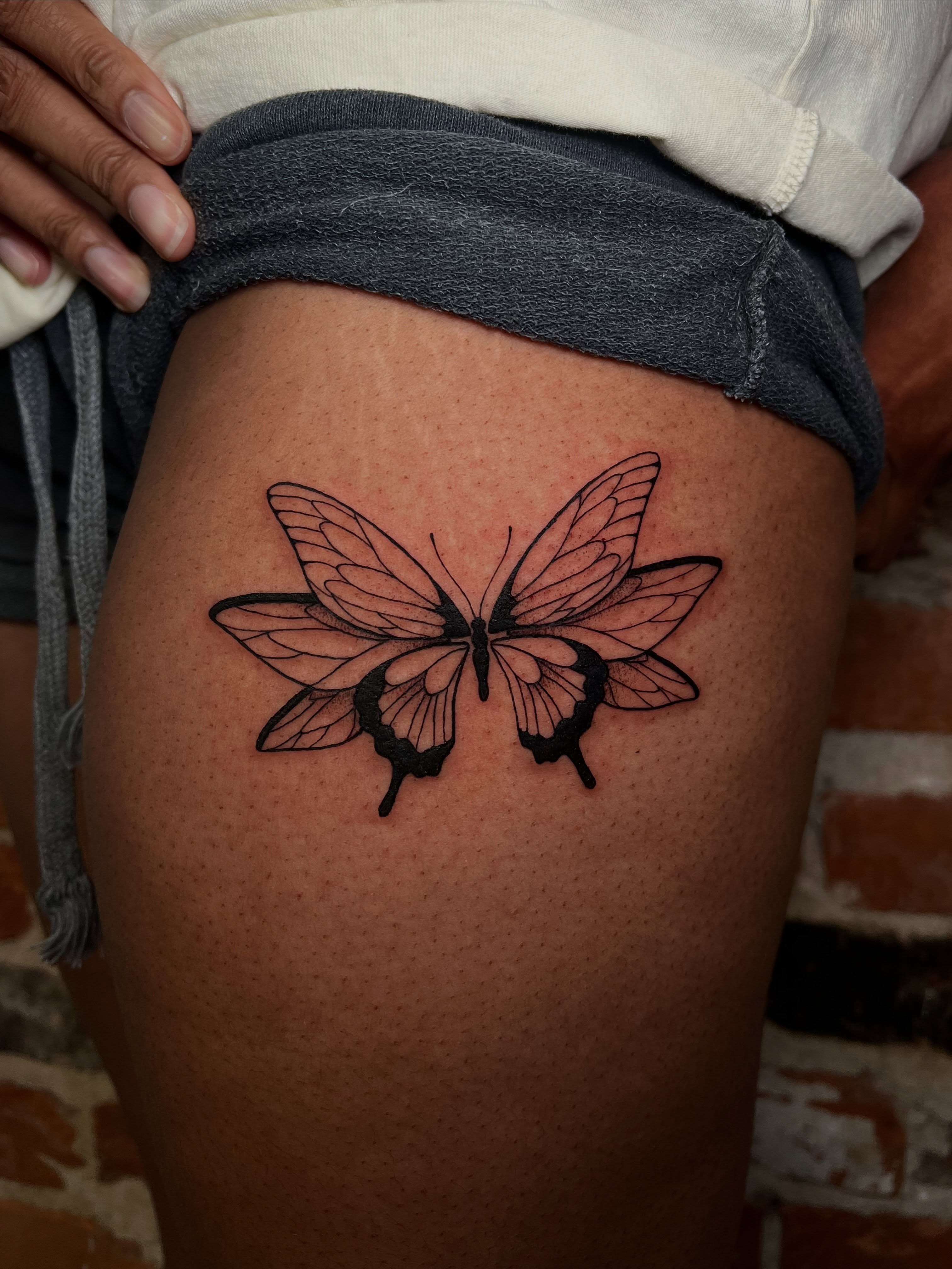 Butterfly black and grey tattoo on the thigh by Uncomfy Comfort Tattoos LLC
