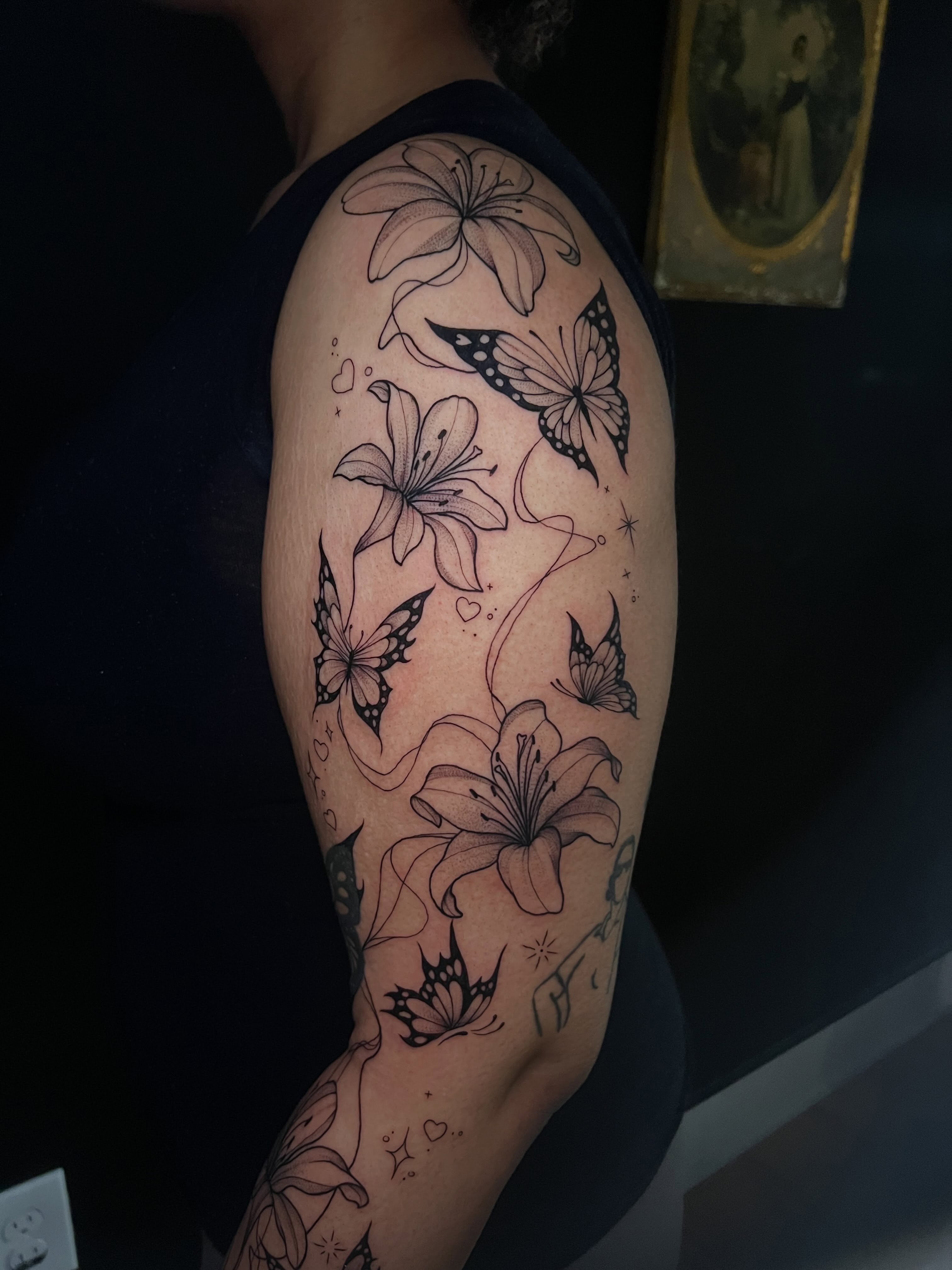 Lilies and butterflies black and grey tattoo on the upper arm by Baung Ben