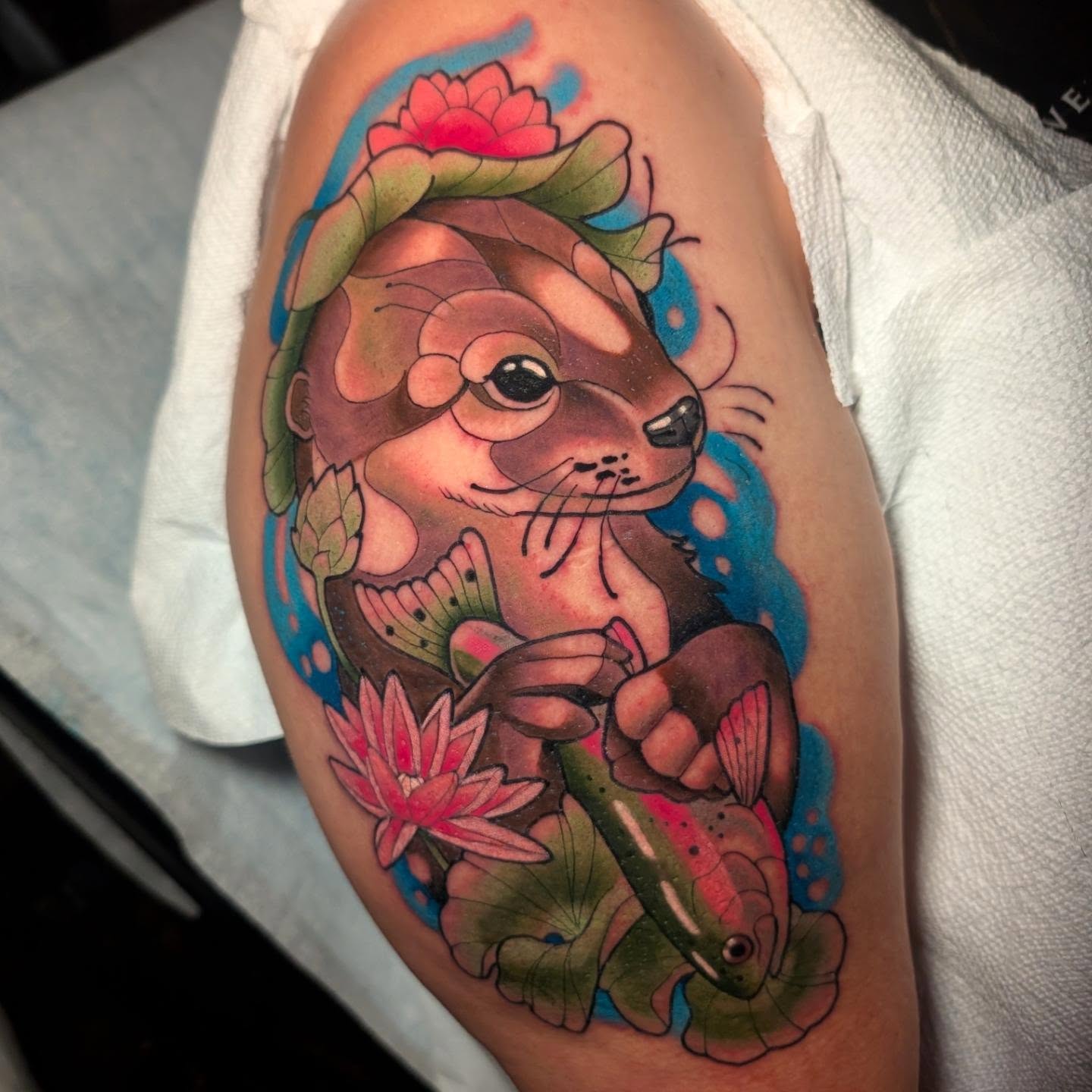 Otter with fish new school tattoo on the upper arm by Ellie