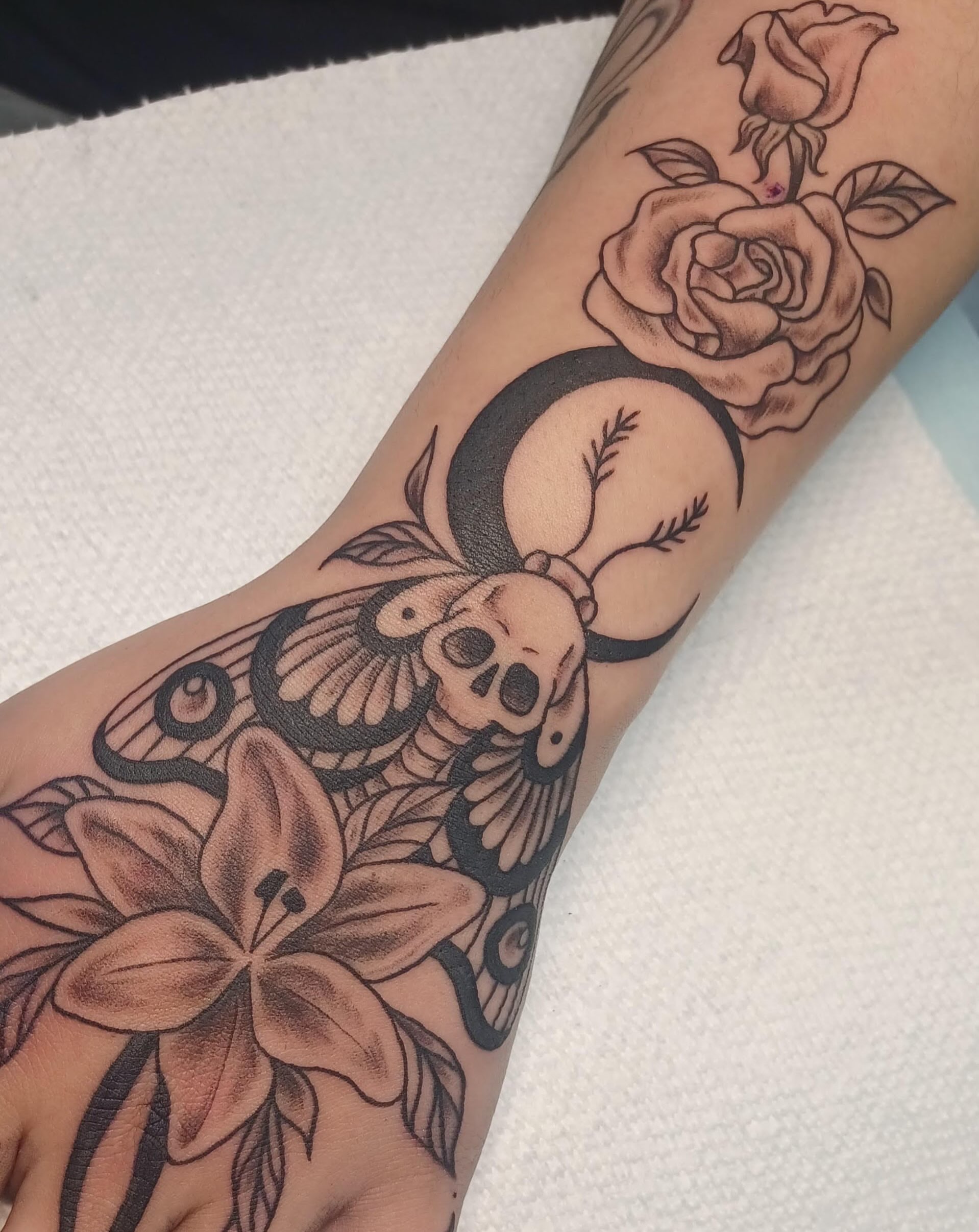 Skull and flowers American traditional tattoo on the forearm by Abi