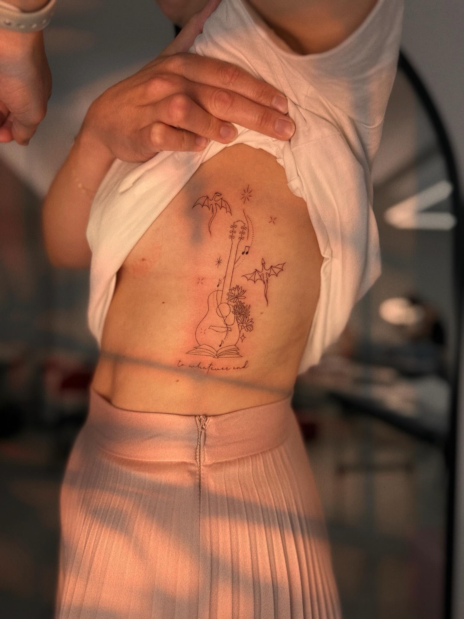 Guitar and book fine line tattoo on the ribs by Ellie