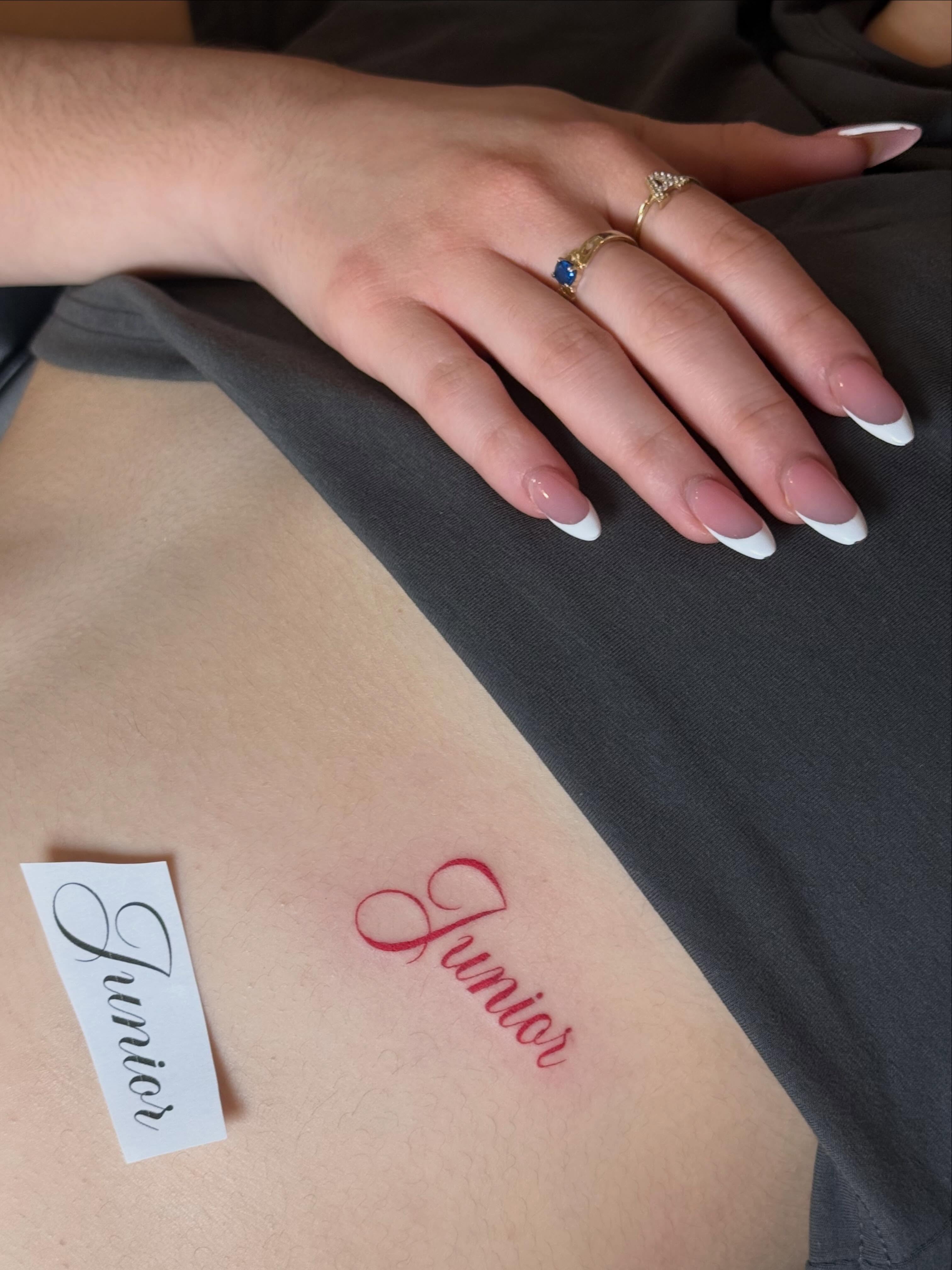 Junior lettering script tattoo on the upper arm by TATTOO & PIERCING ARTIST ₊˚⊹ ᰔ