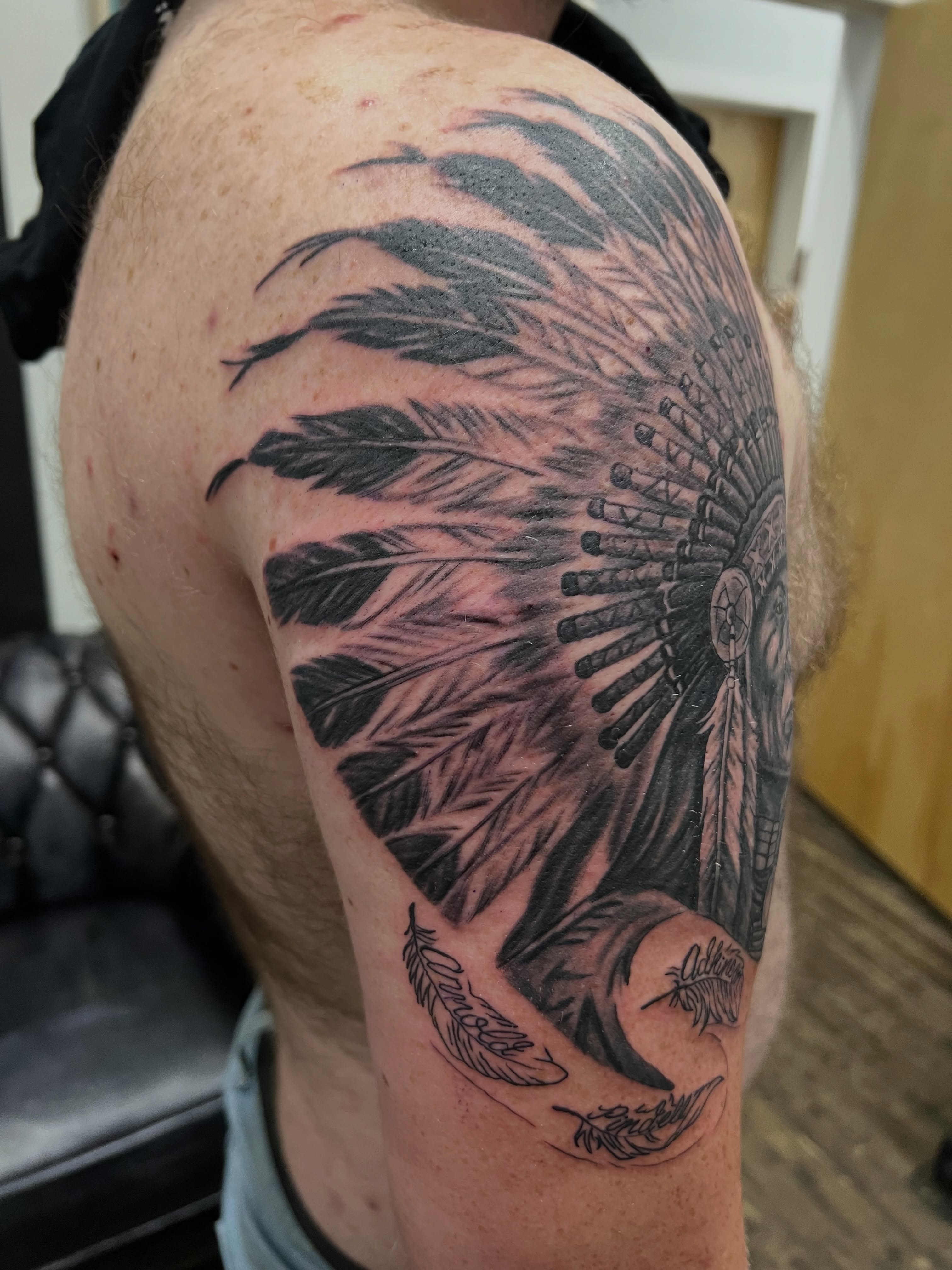 Feather headdress black and grey tattoo on the shoulder by A.W.