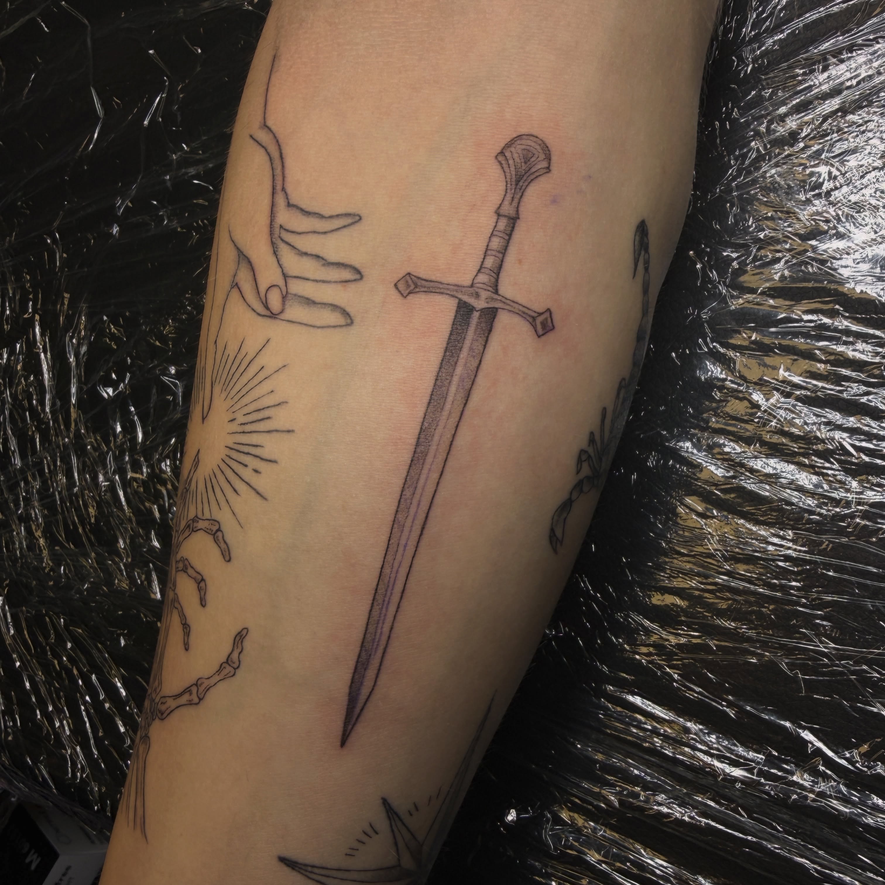 Sword and hand black and grey tattoo on the forearm by Pretty Ugly Tattoos