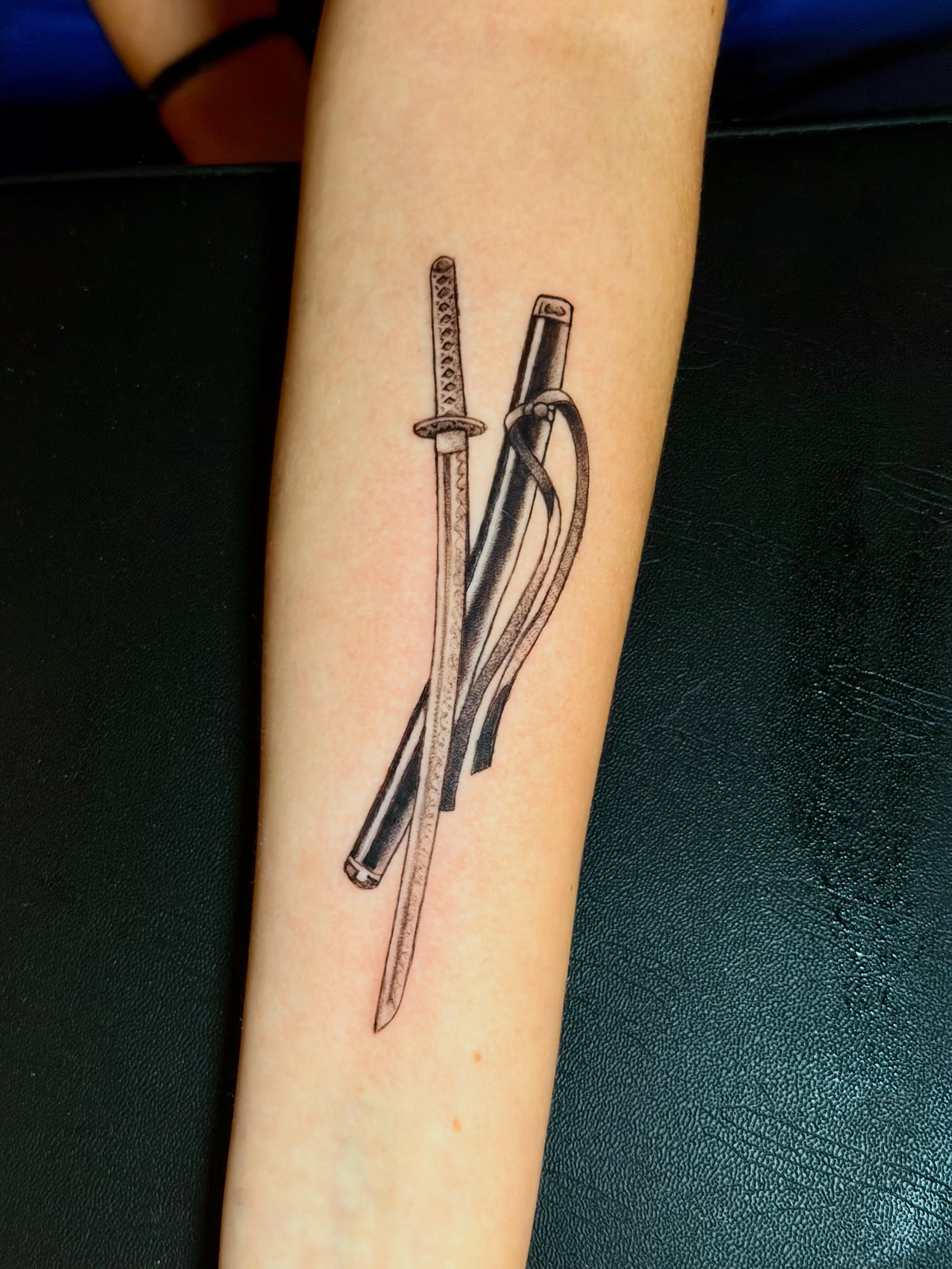 Katana and sheath black and grey tattoo on the forearm by C.J.K. Roy