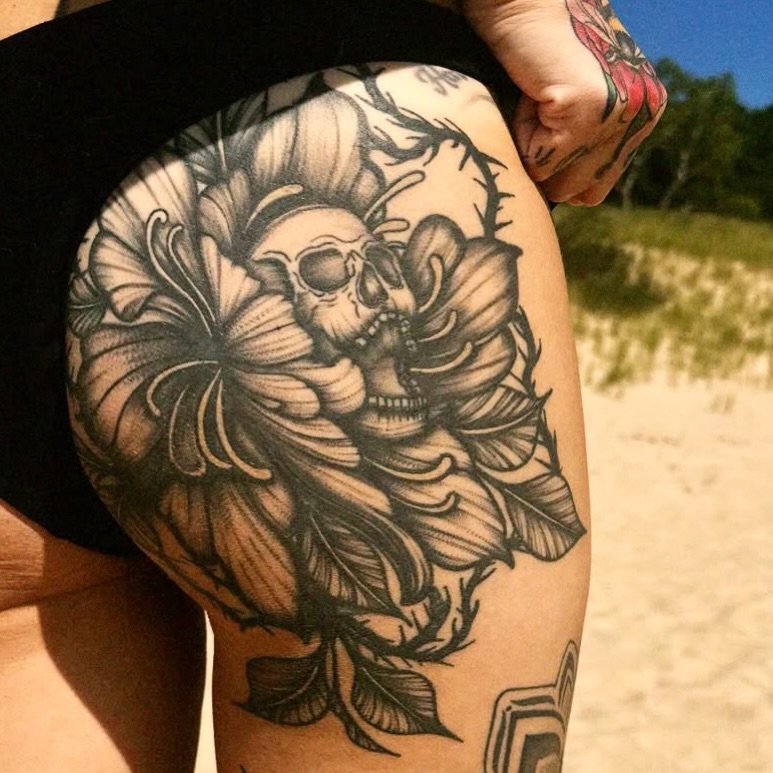 Skull and flower black and grey tattoo on the thigh by Kirsten Cameron