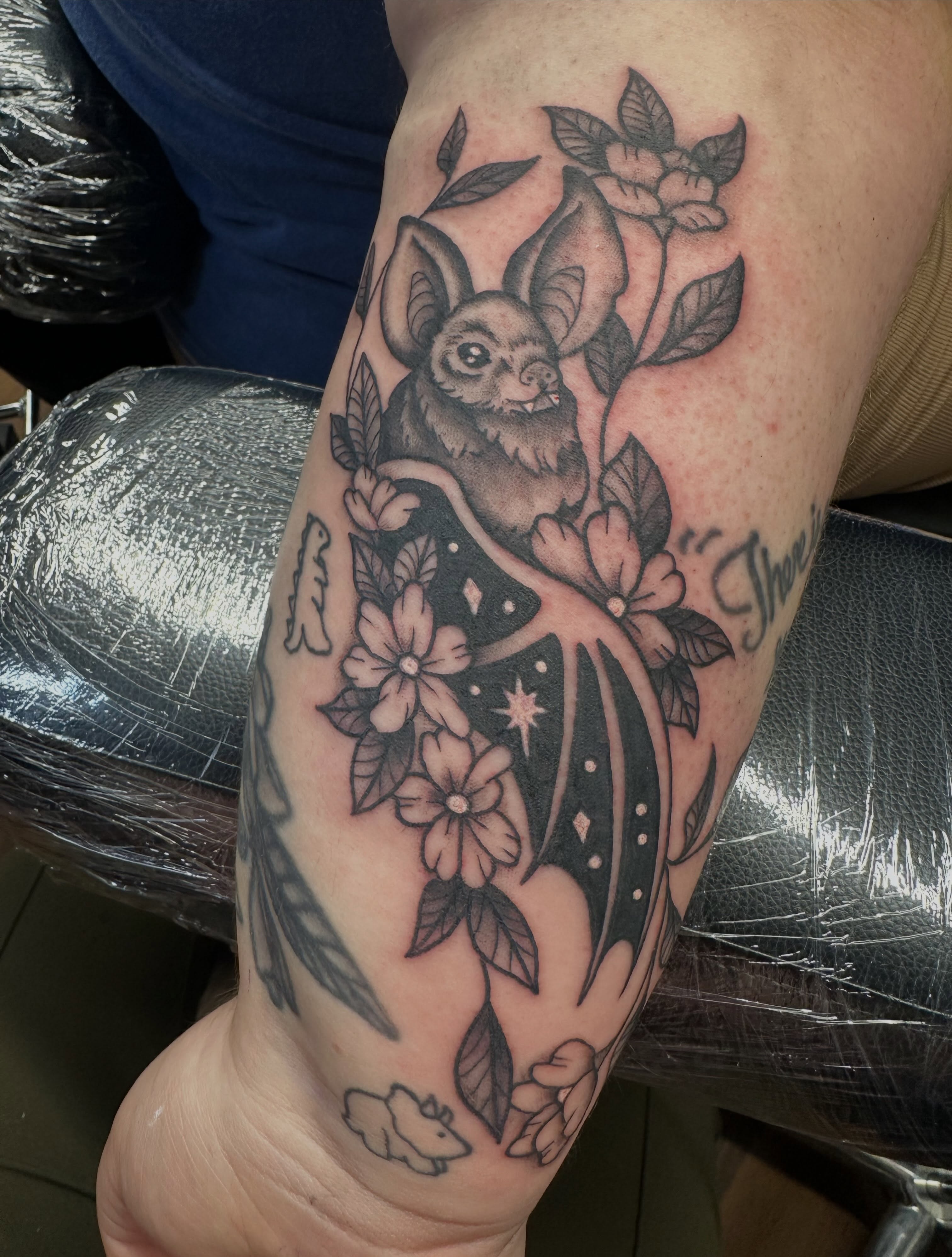 Bat and flowers black and grey tattoo on the forearm by Lindsey Bendsey