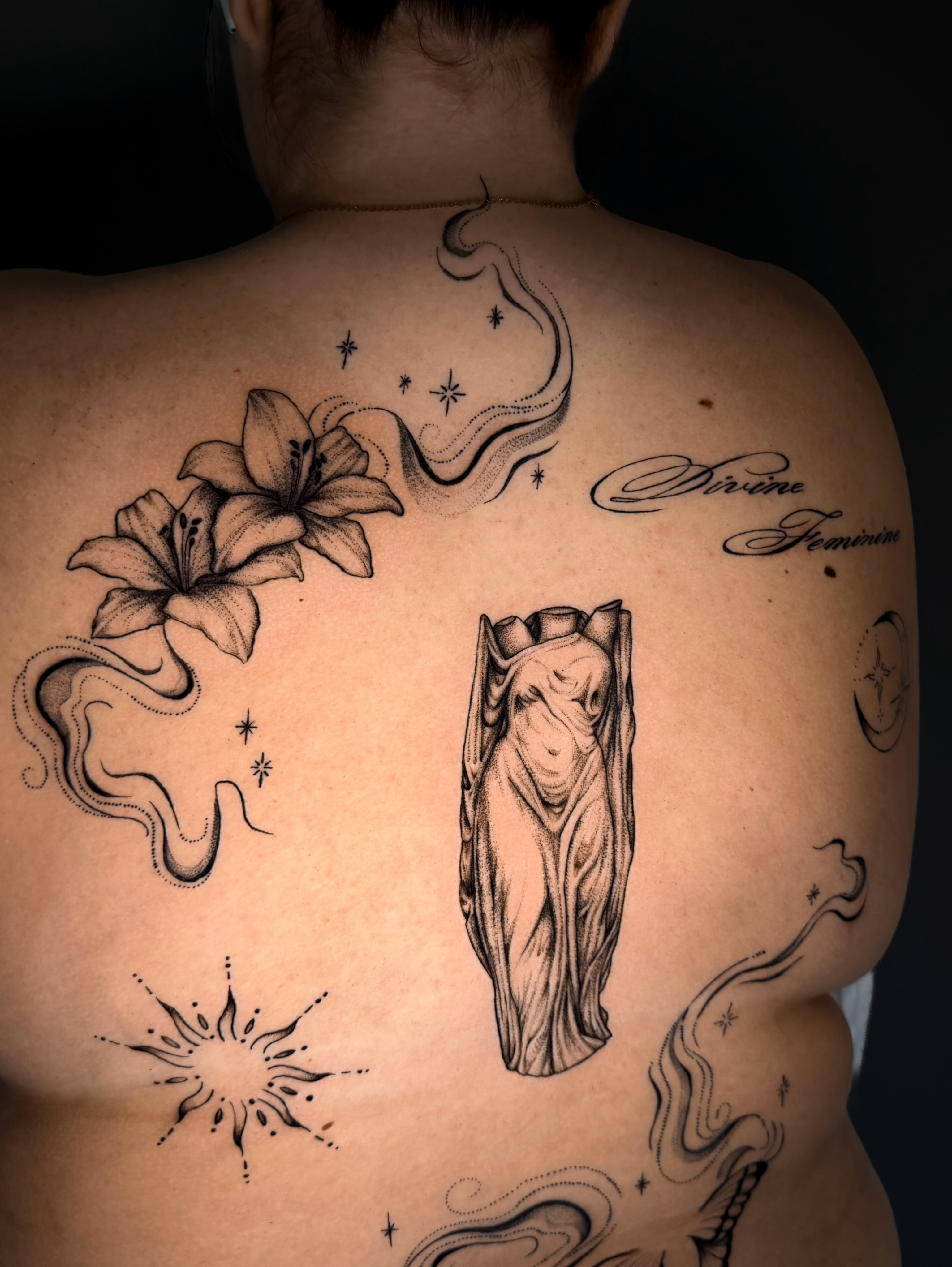 Statue and lilies realism tattoo on the back by Kam Mills