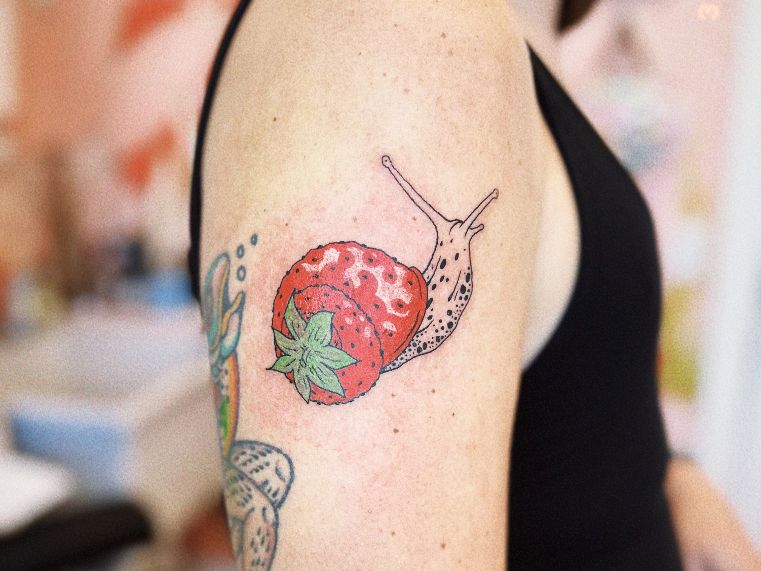 Snail and strawberry realism tattoo on the upper arm by Emma Berger
