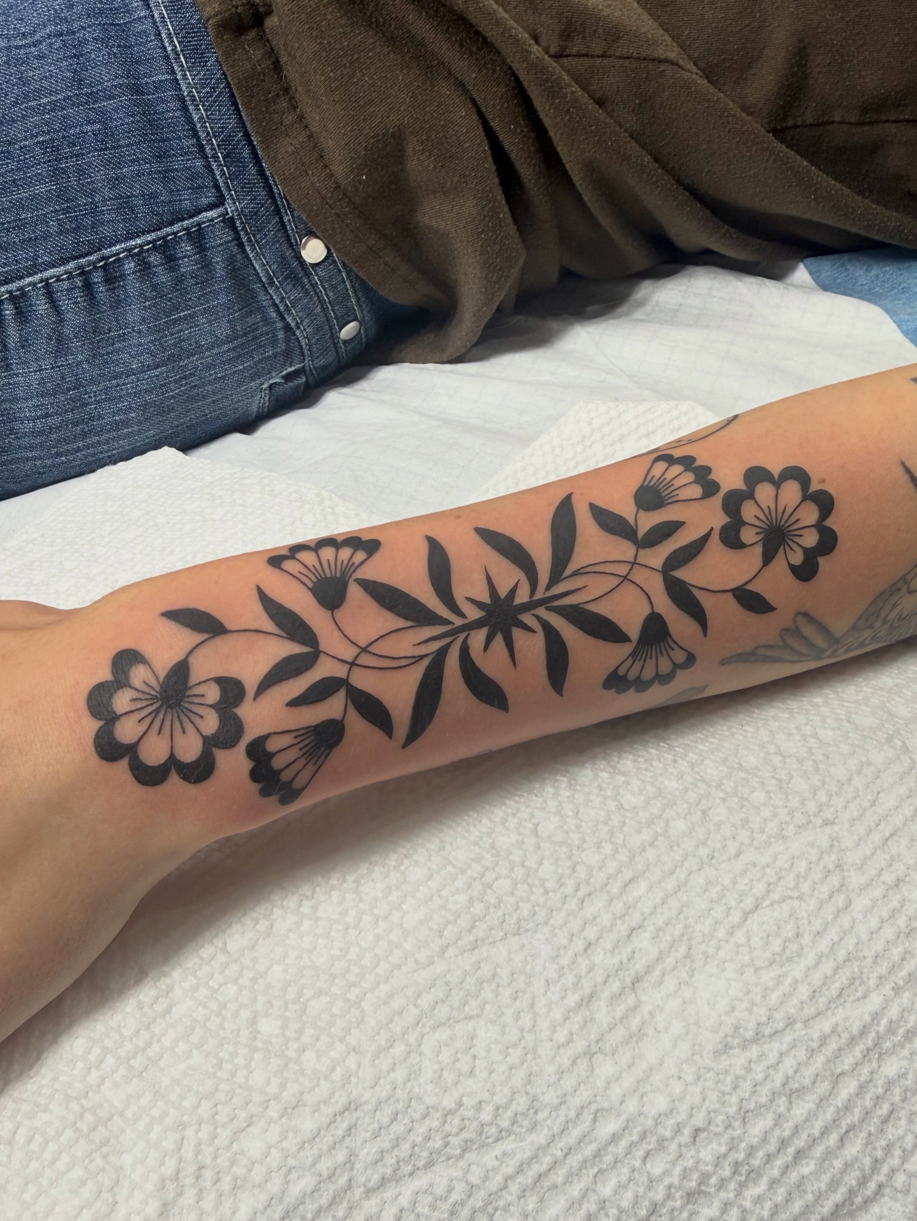 Floral arrangement black and grey tattoo on the forearm by Maddie Jo DeYoung