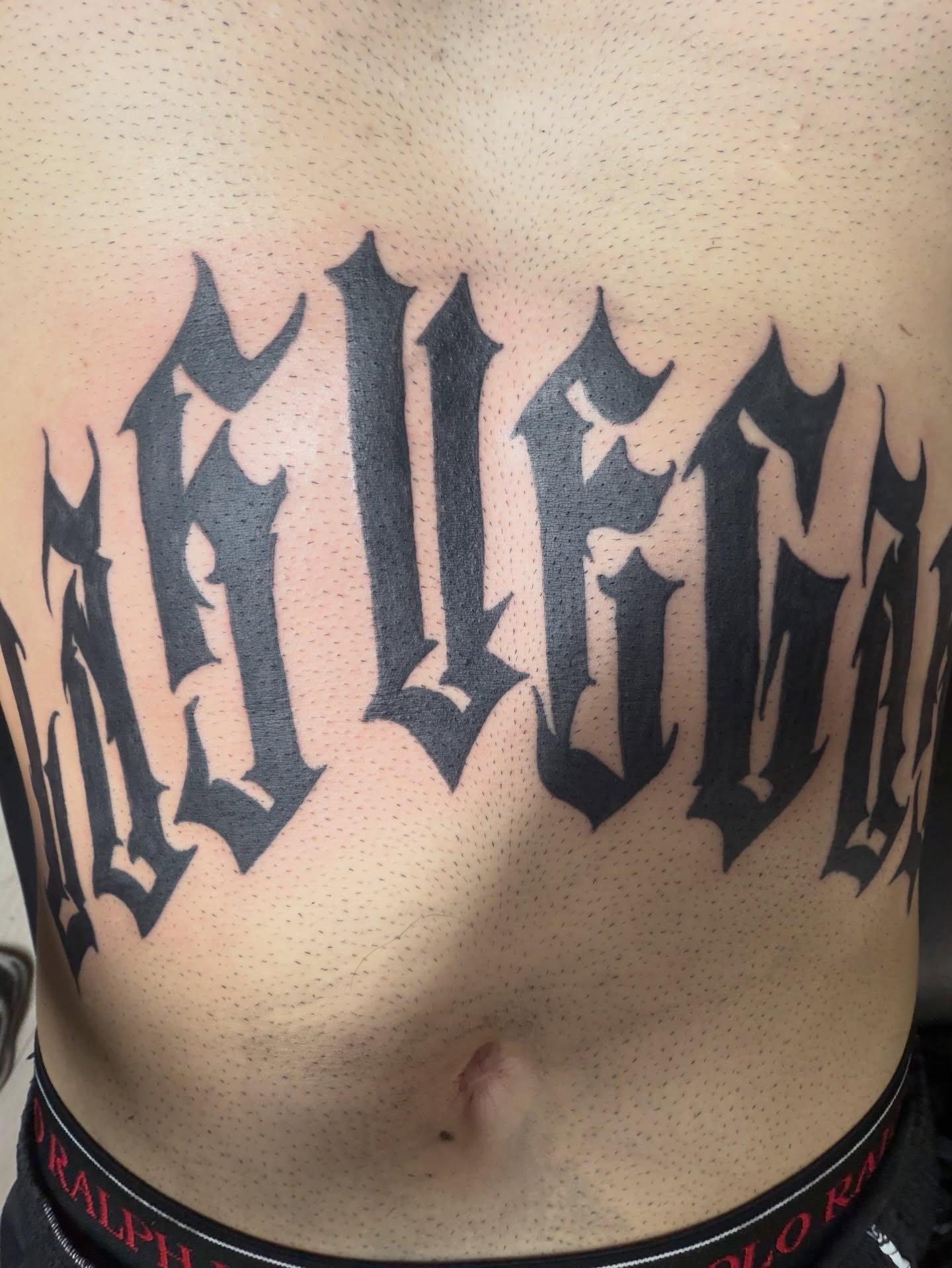 Gothic lettering tattoo on the chest by Marky