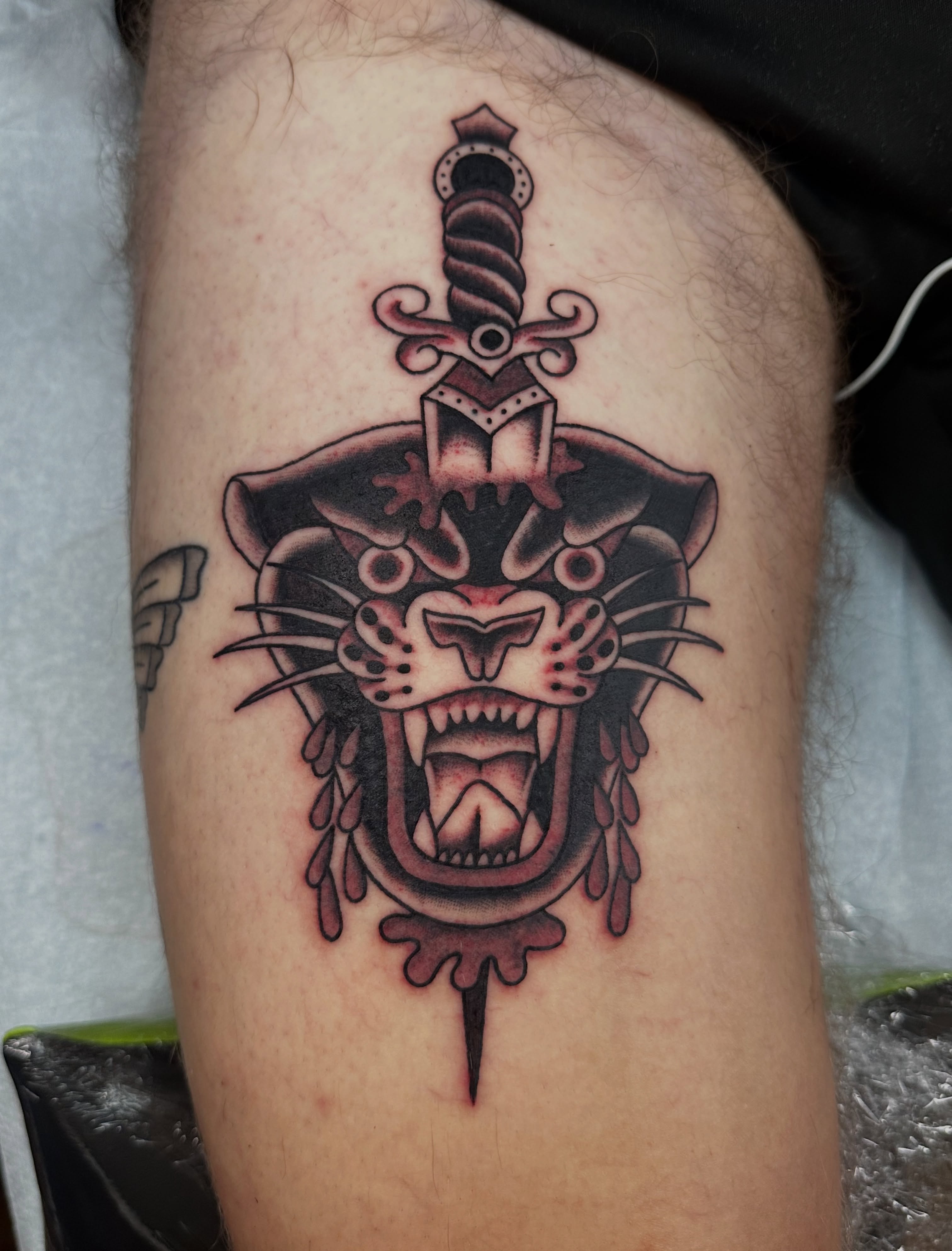 Panther head with sword American traditional tattoo on the thigh by Emily Masa