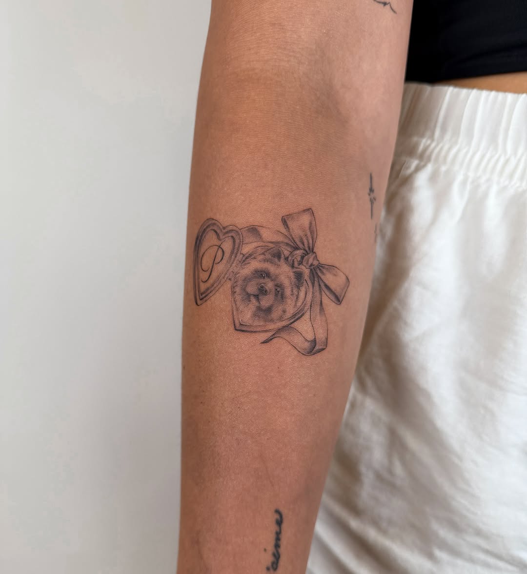 Locket with dog and initial P minimalist tattoo on the forearm by Helly March