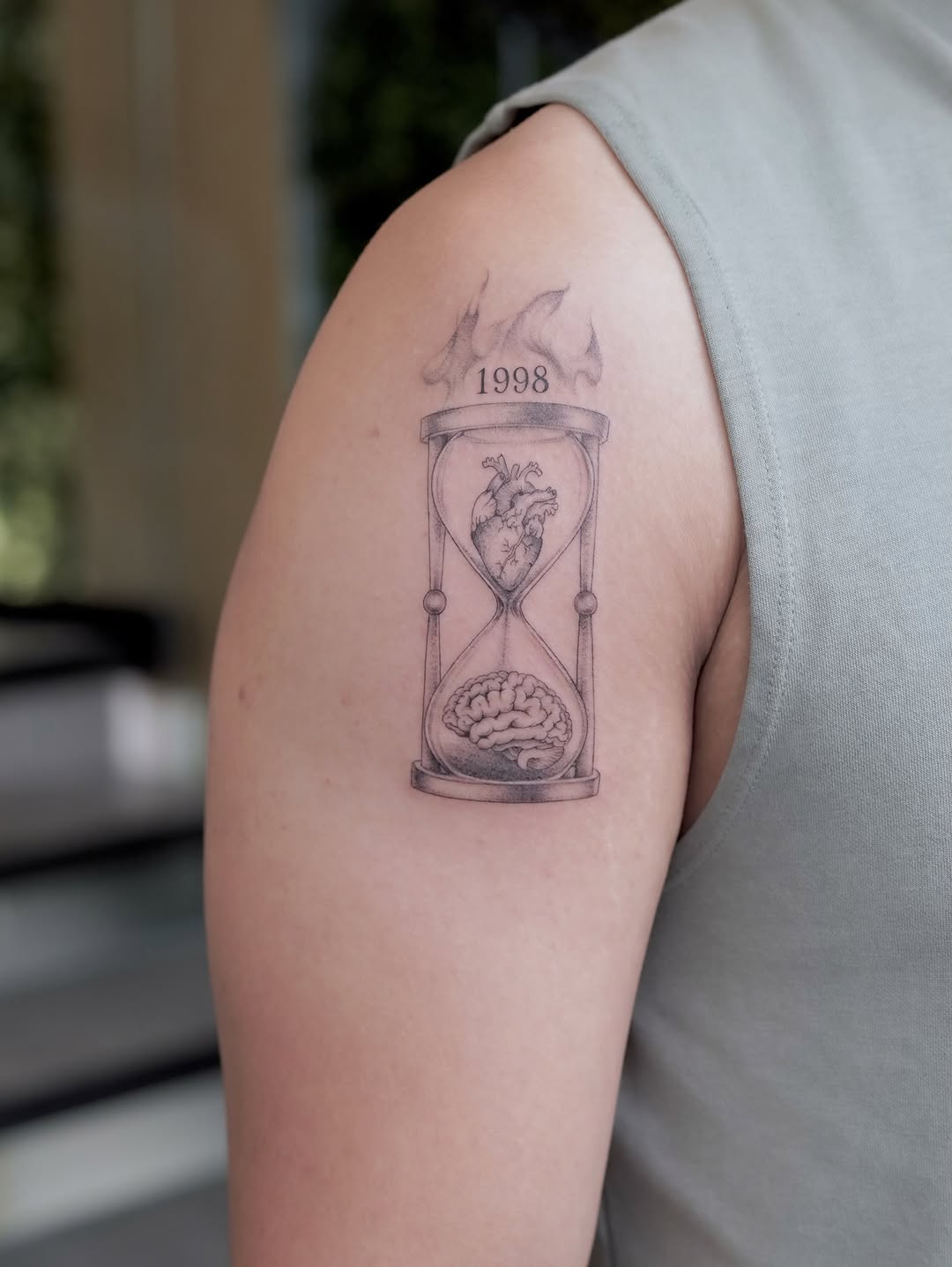 Hourglass with heart and brain surrealism tattoo on the upper arm by Julia
