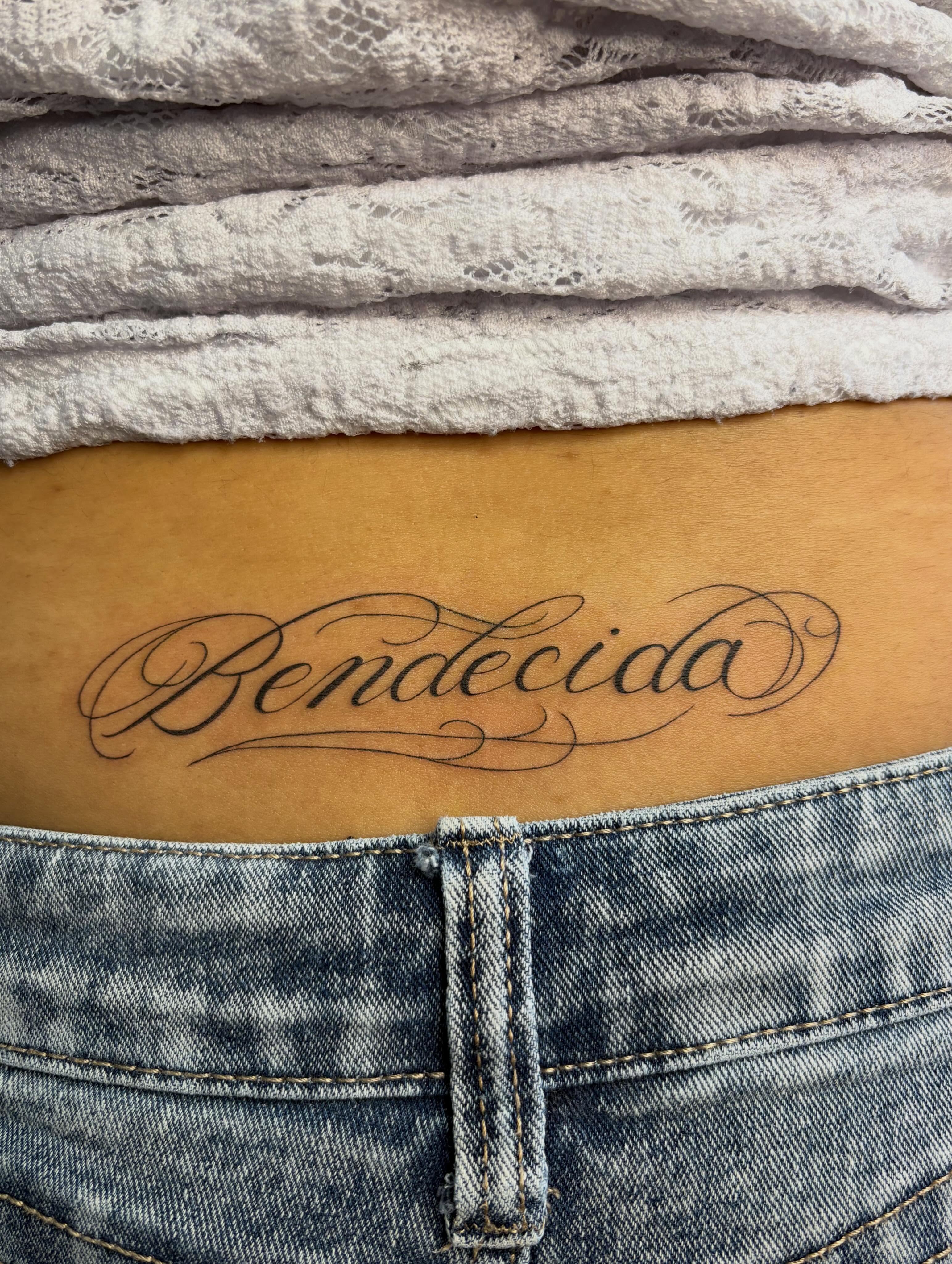 Bendecida lettering script tattoo on the thigh by alana khounmeuang