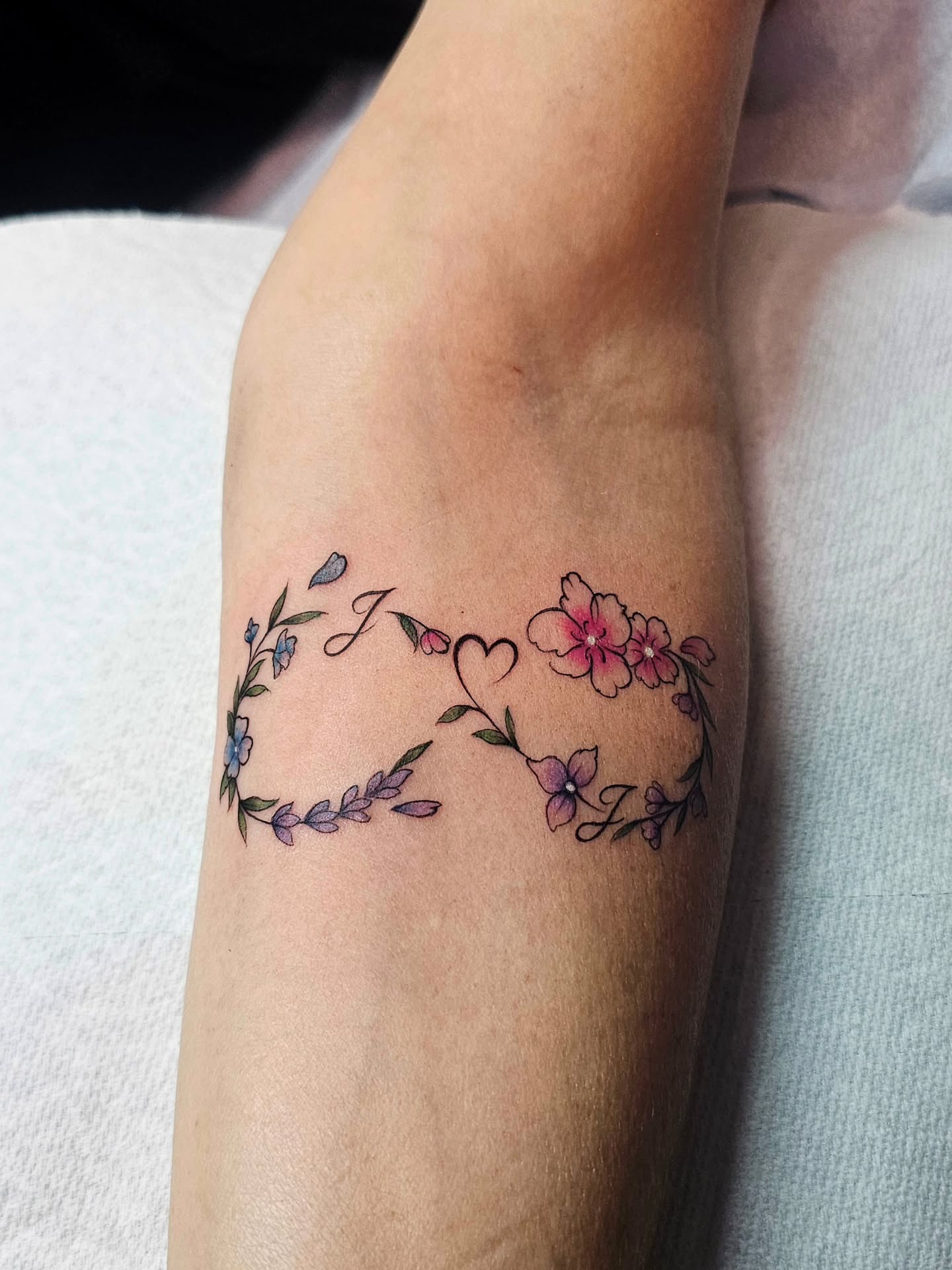Floral wreath with initials fine line tattoo on the forearm by Adriannah Esparza