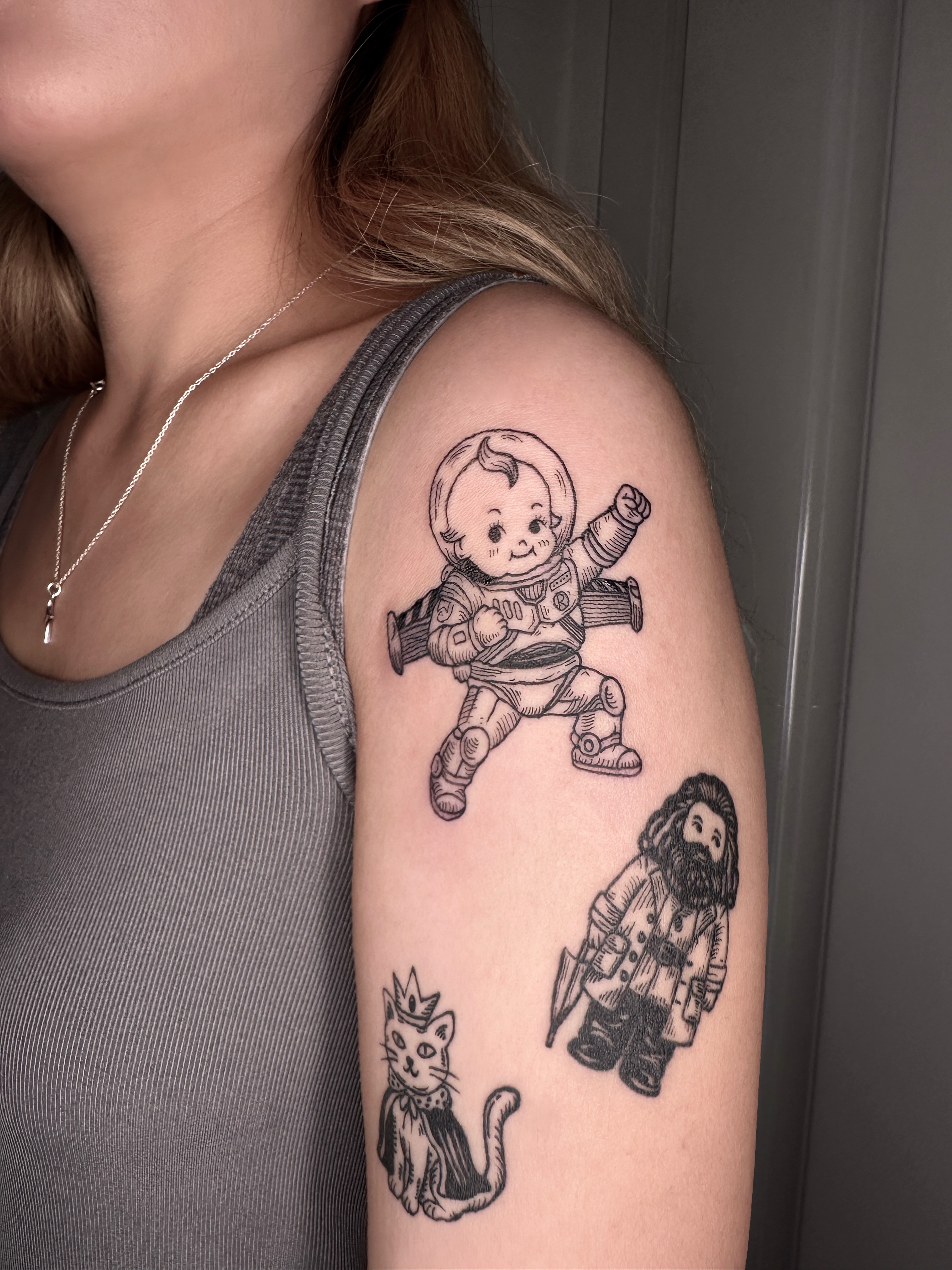 Astronaut baby, cat, wizard black and grey tattoo on the upper arm by Zecember
