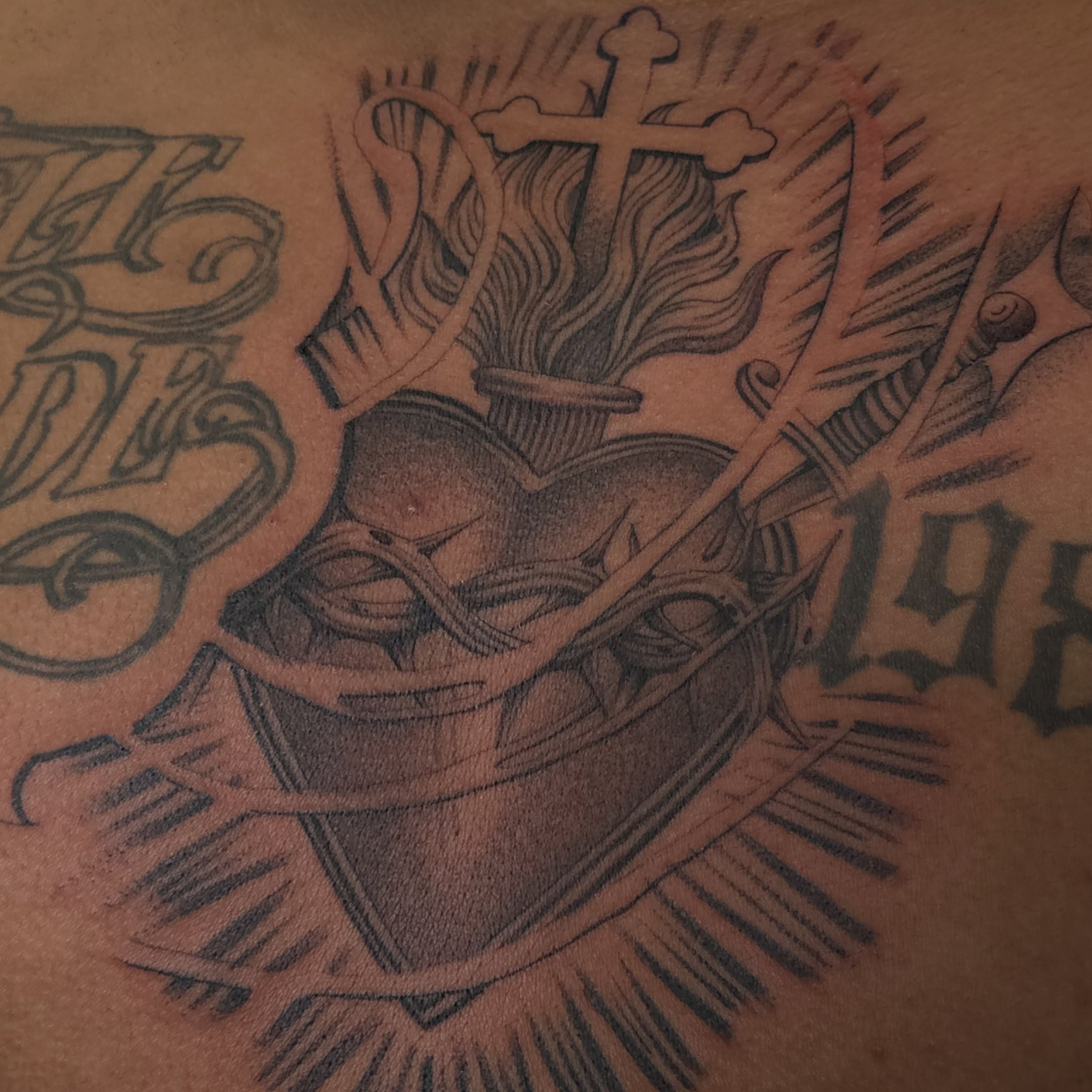 Heart with cross black and grey tattoo on the chest by San Diego Tattoo Artist
