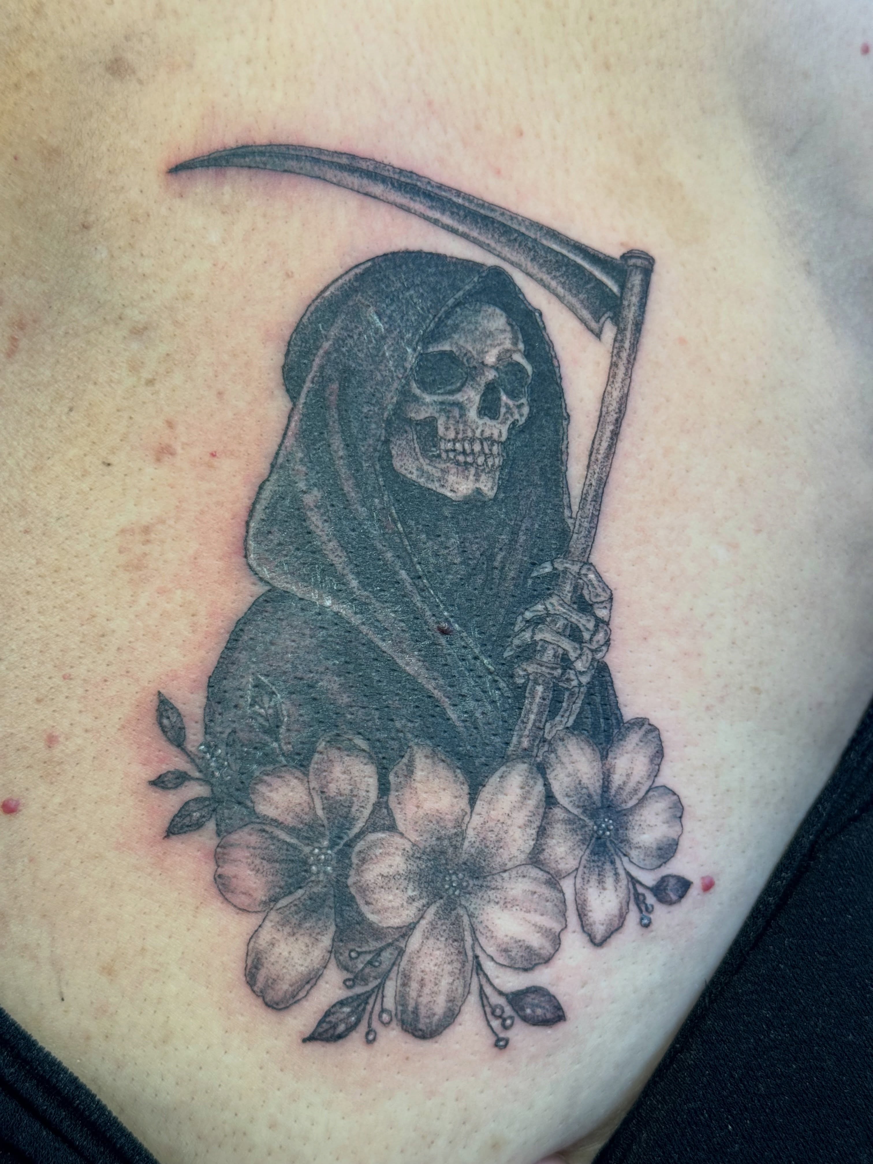 Grim reaper with flowers black and grey tattoo on the chest by Ink Napawong