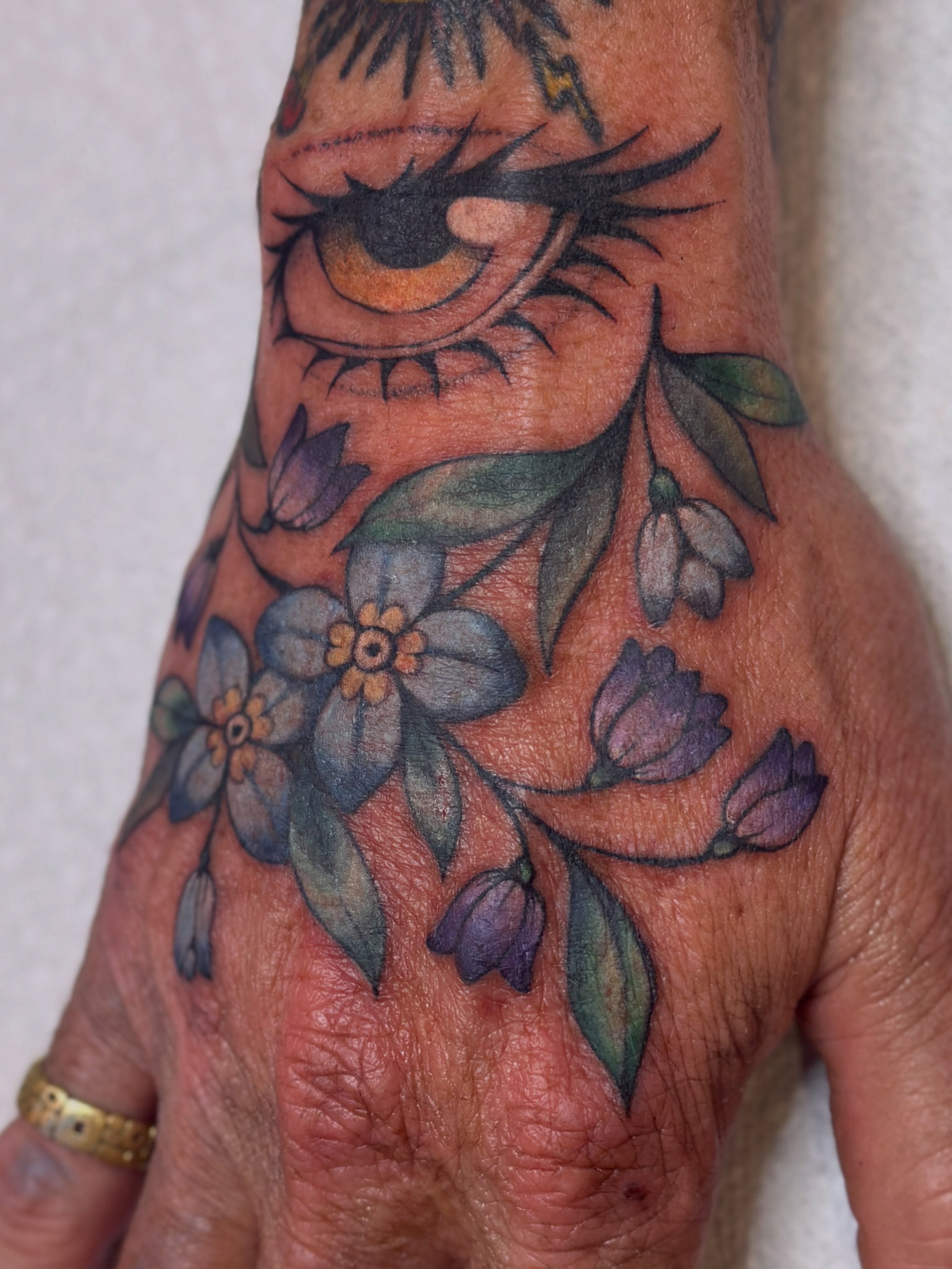 Eye and floral bouquet realism tattoo on the hand by Dani Di Pietrantonio